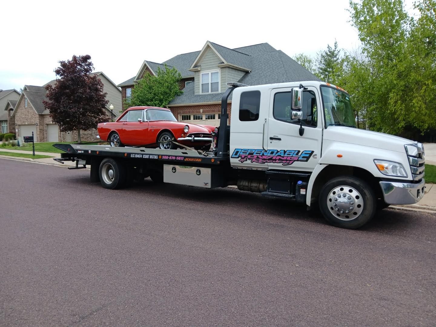 White tow truck carrying a red car on a suburban street