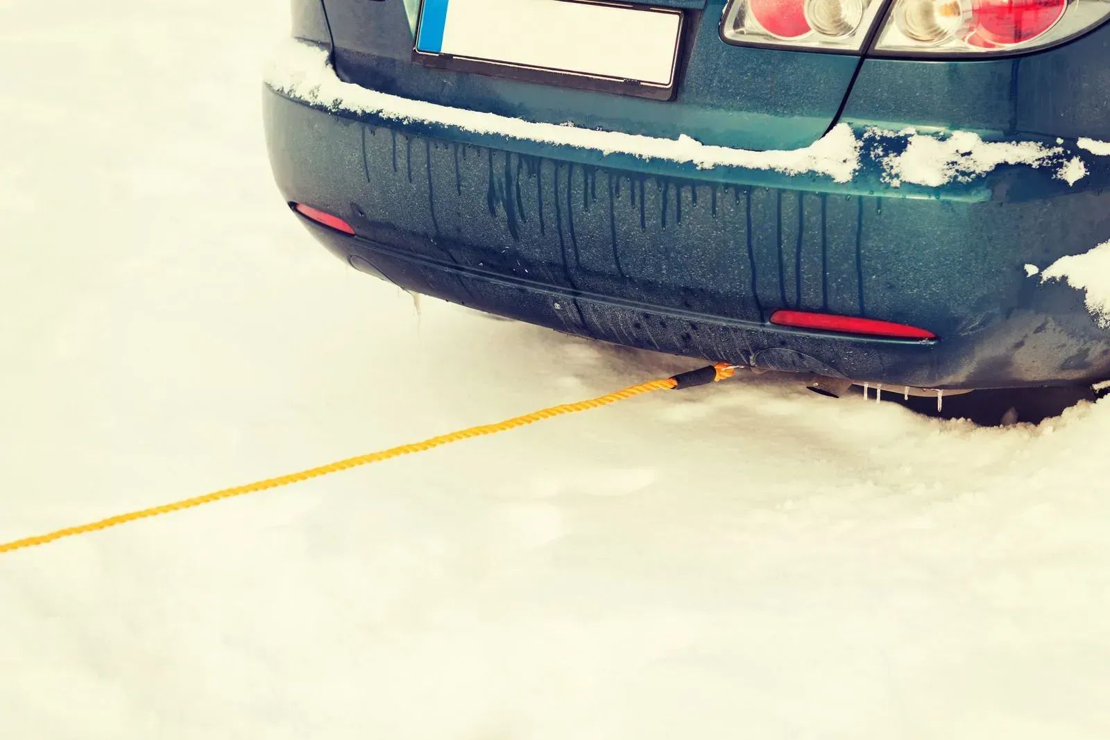 Rear of a dark green car stuck in snow, with a yellow tow strap attached underneath.