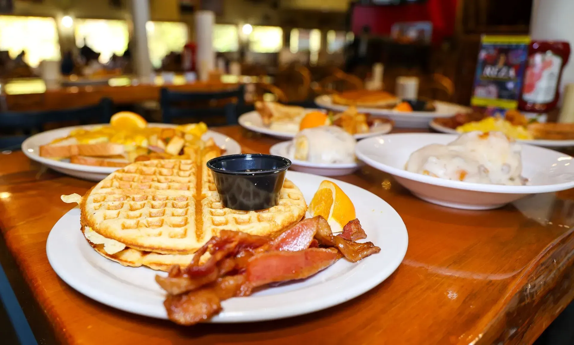 A table topped with plates of food including waffles , bacon and eggs.