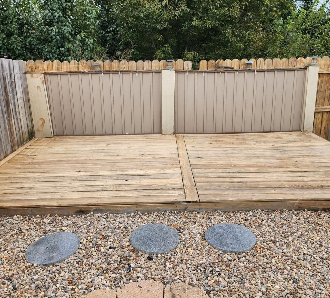 There is a wooden deck in the backyard with a fence in the background.