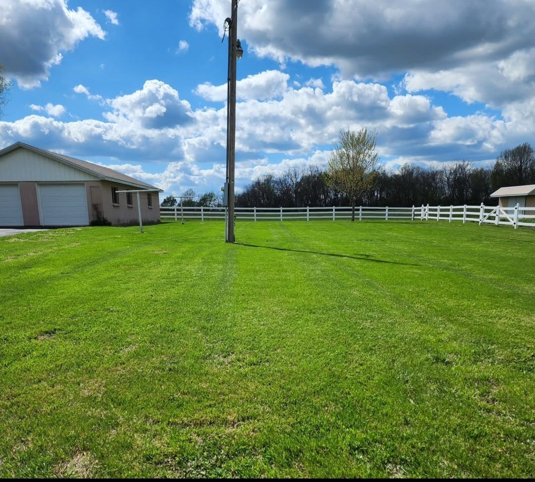 A lush green field with a house in the background and a fence in the foreground.