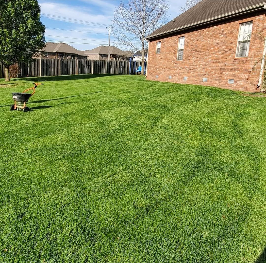 A lush green lawn in front of a brick house with a wheelbarrow in the foreground.