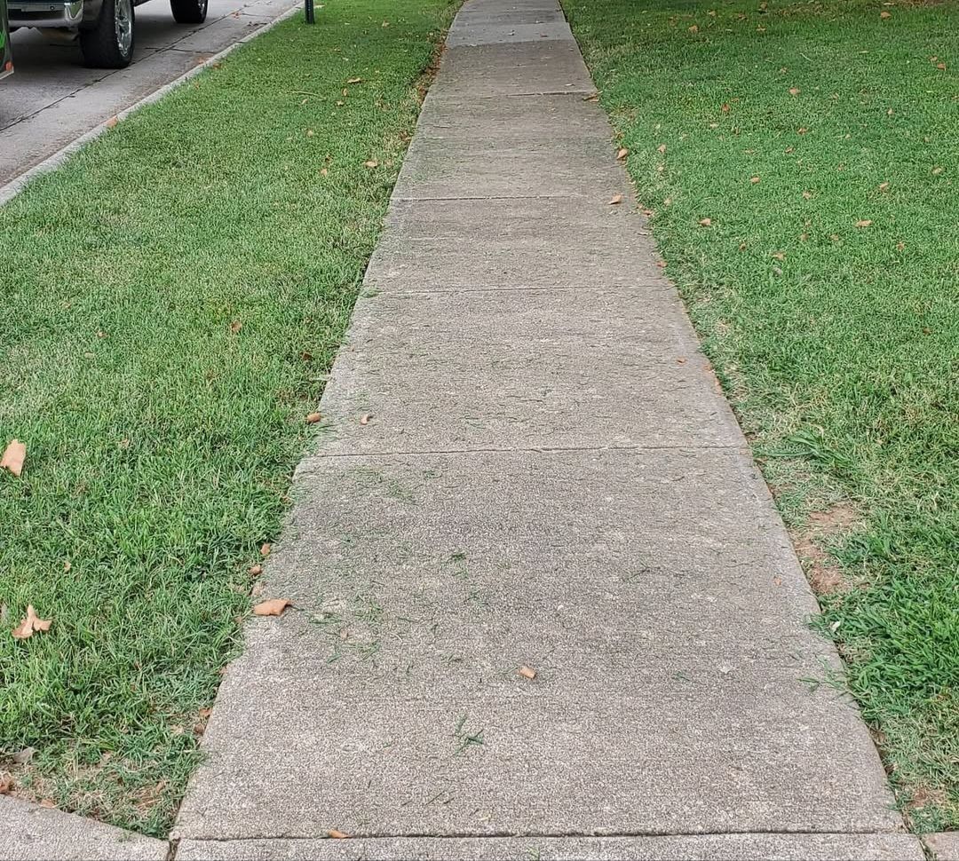 A sidewalk leading to a grassy yard with a truck parked on the side of the road.