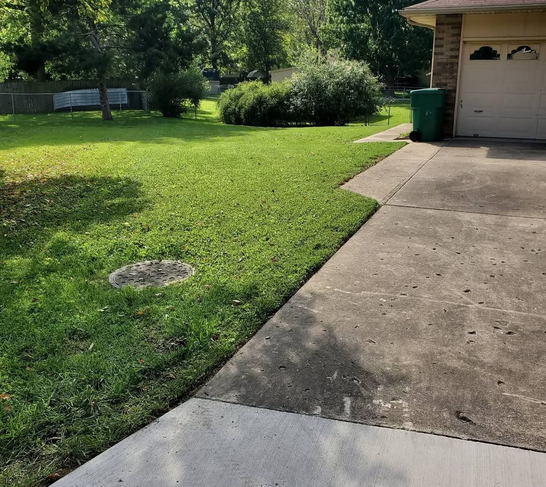A concrete walkway leading to a house with a green trash can in front of it.