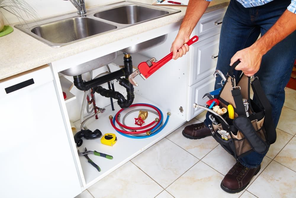 Plumber Is Fixing A Sink In A Kitchen — Russell Plumbing In Manunda, QLD