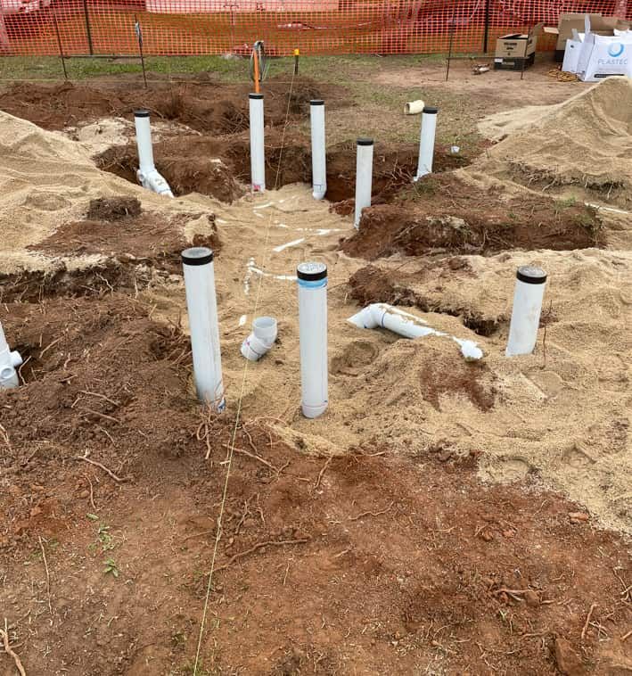 A Bunch Of White Pipes Are Sitting In The Dirt — Russell Plumbing In Gordonvale, QLD