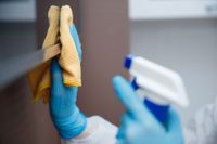 Person wearing blue gloves, cleaning with spray bottle and yellow cloth.