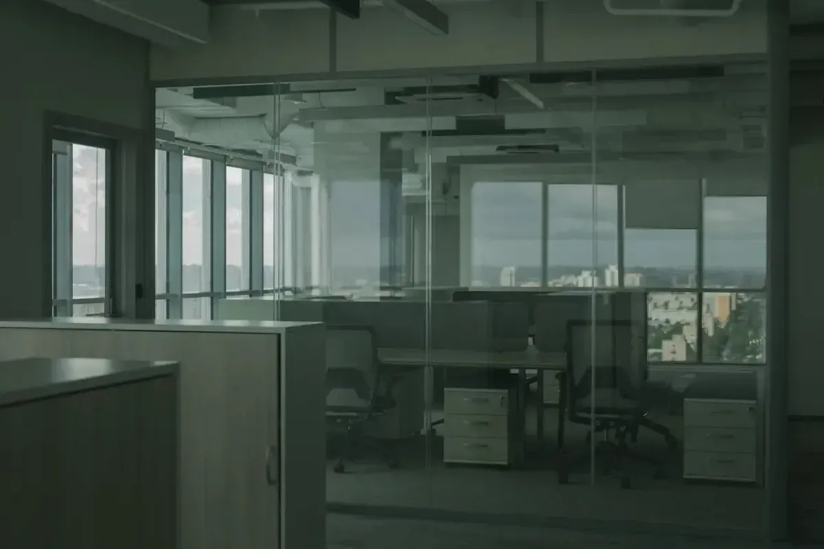 Empty office interior with glass walls, desks, and city views.