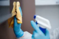 Person wearing blue gloves, cleaning with spray bottle and yellow cloth.