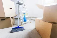 Boxes, ladder, broom, and cleaning spray in an empty room, preparing for a move.