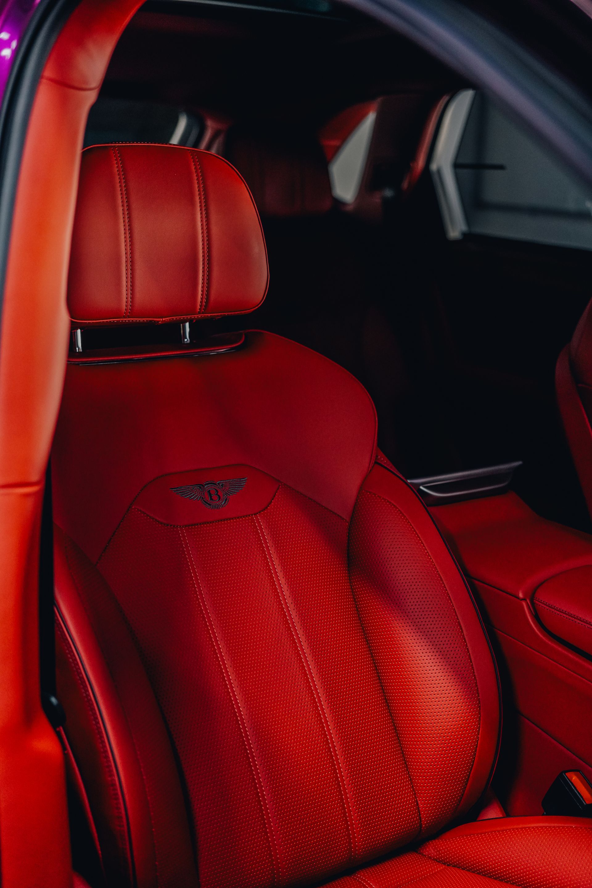 Red leather car seat with a stitched headrest and perforated center panel inside a dark vehicle interior