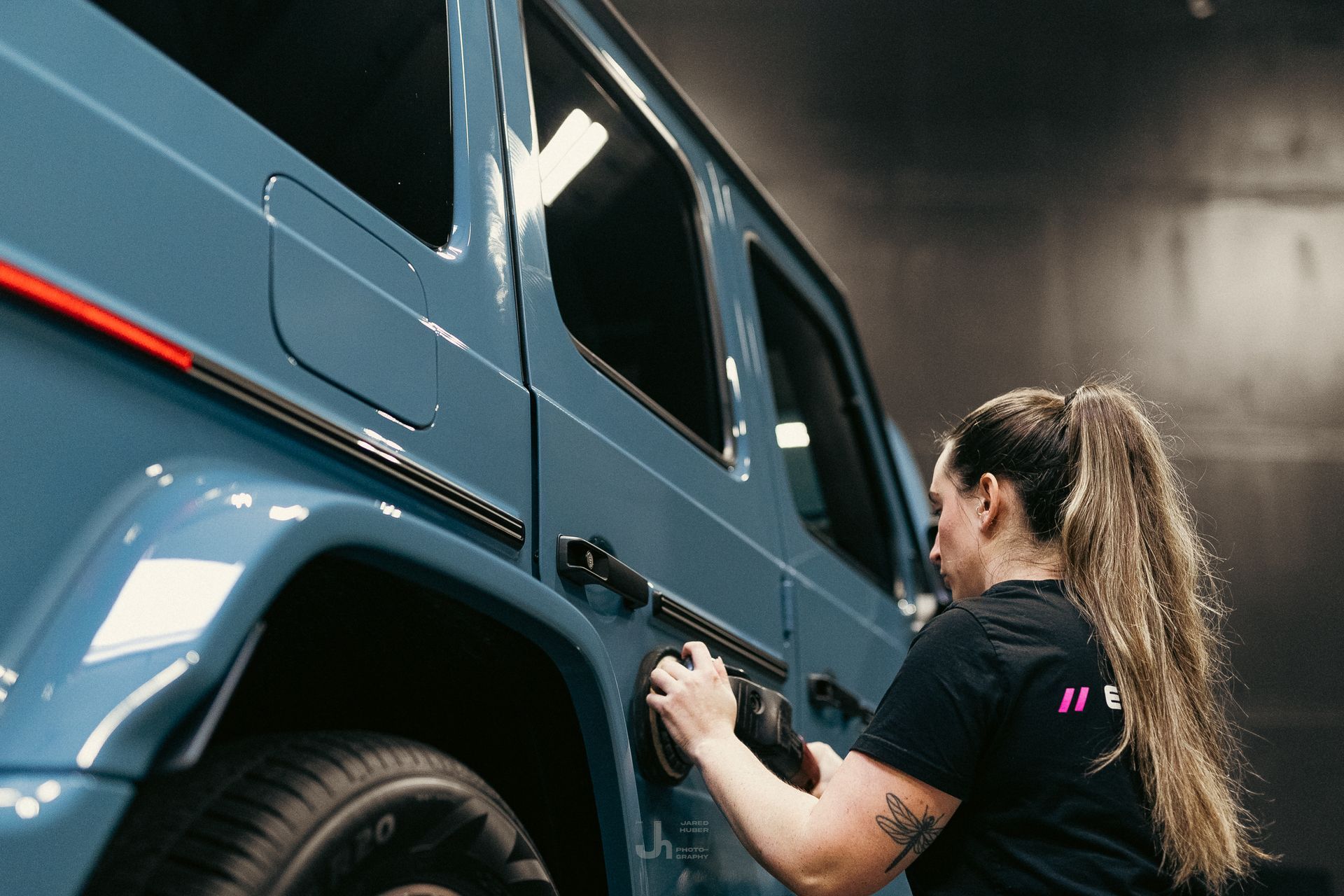 Woman cleaning a blue off-road vehicle in a workshop