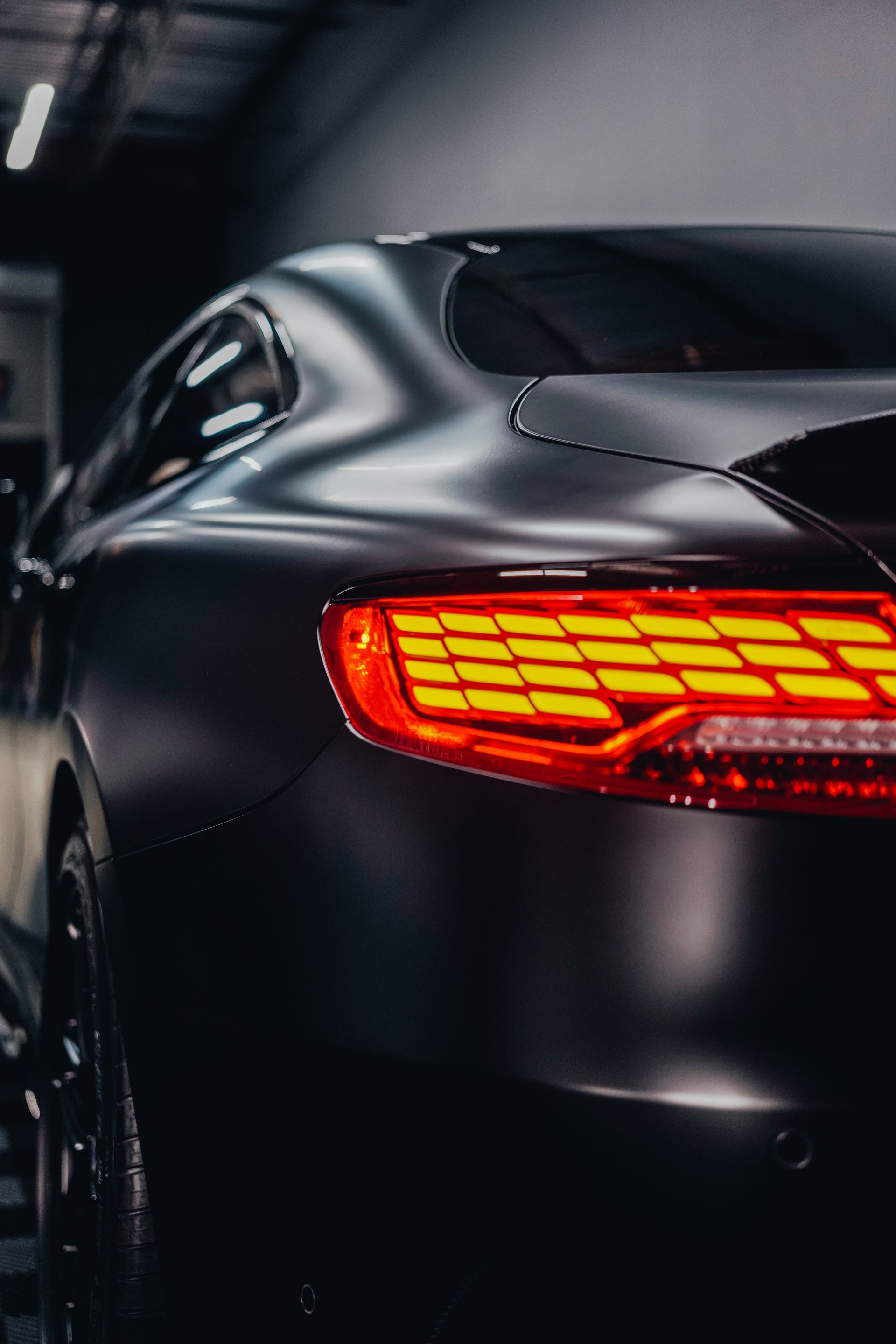 Rear view of a black sports car with glowing red taillight in a dark setting