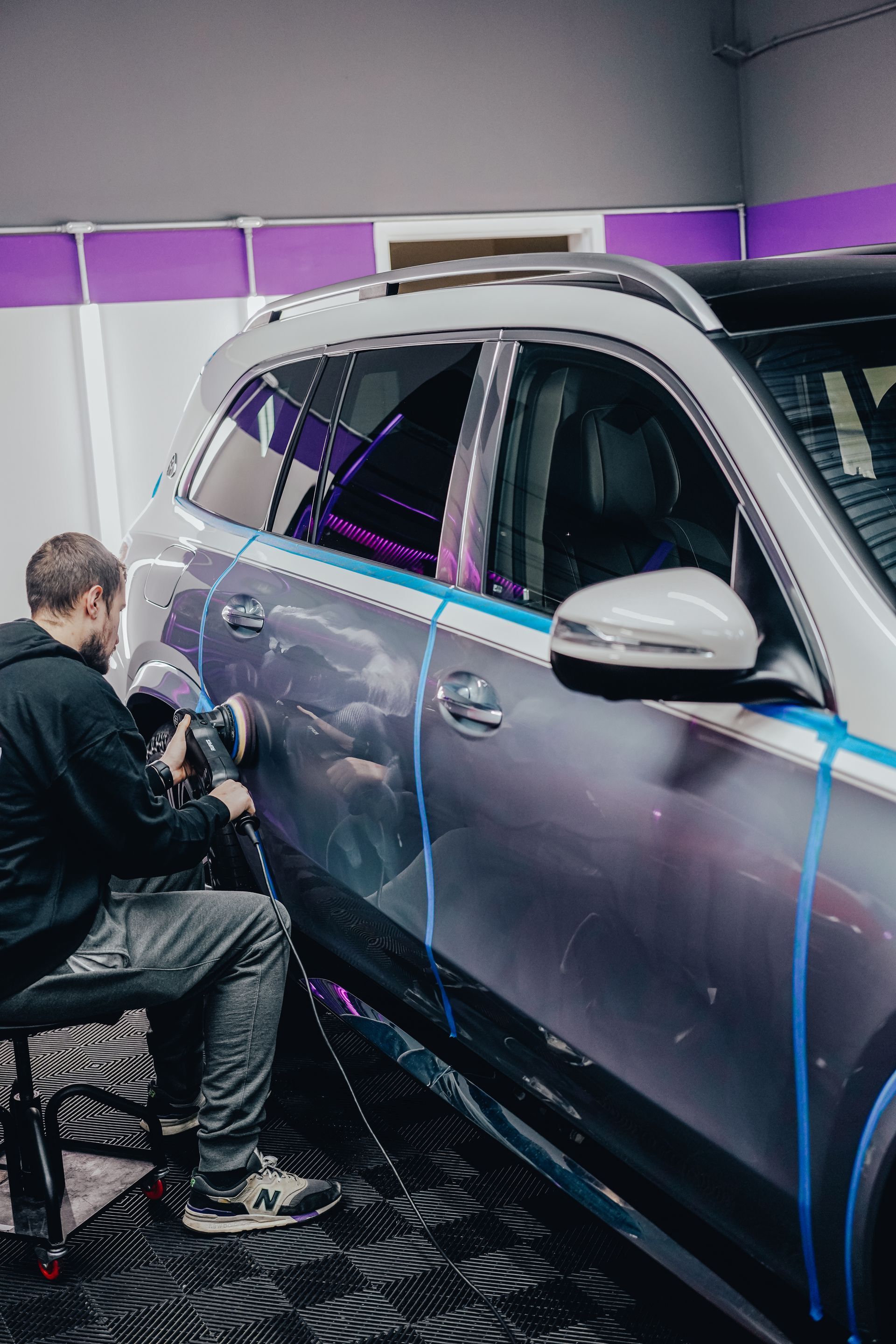 Person polishing a silver SUV in a workshop with purple wall panels
