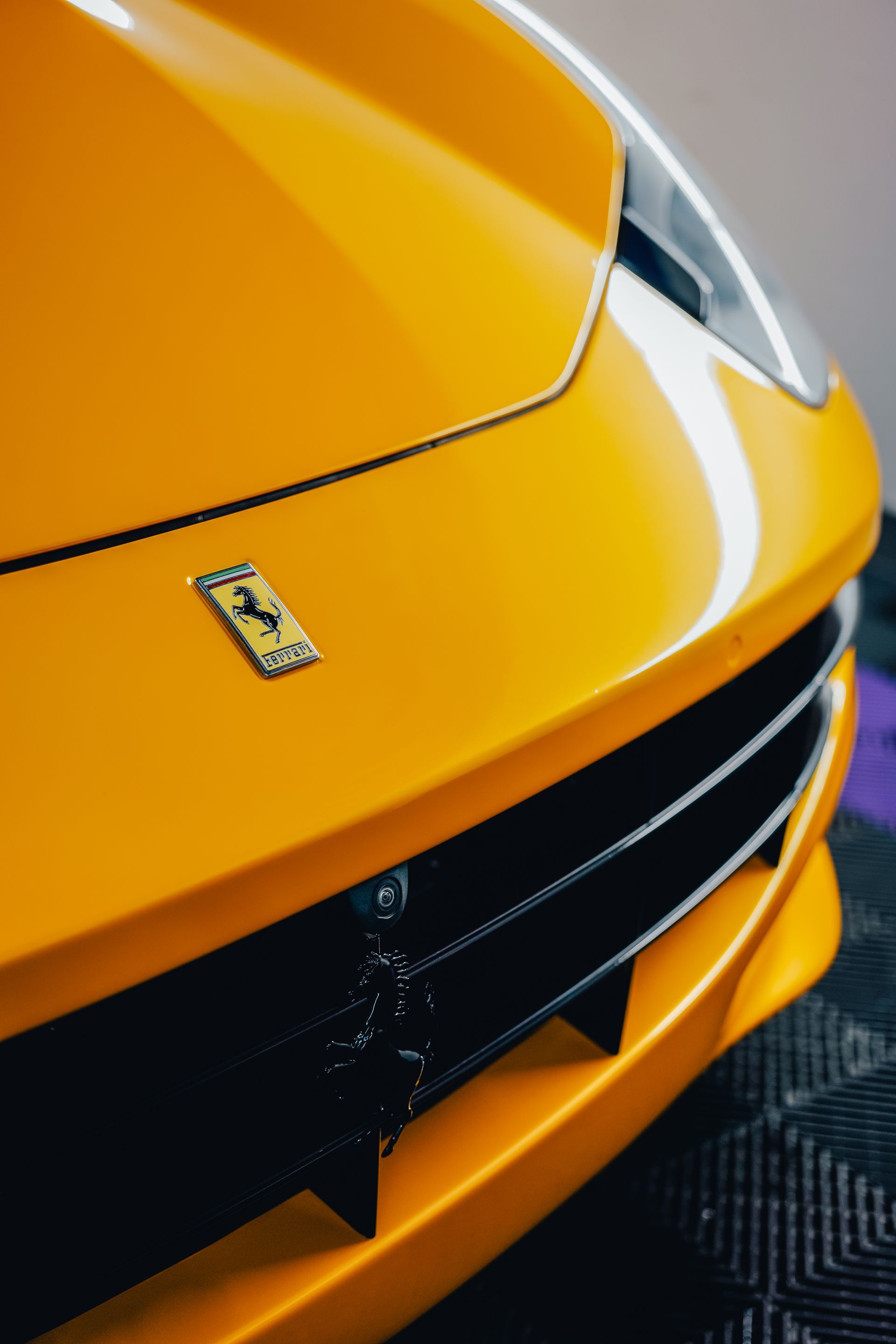 Close-up of the front of a yellow sports car with a Ferrari badge on a dark floor.