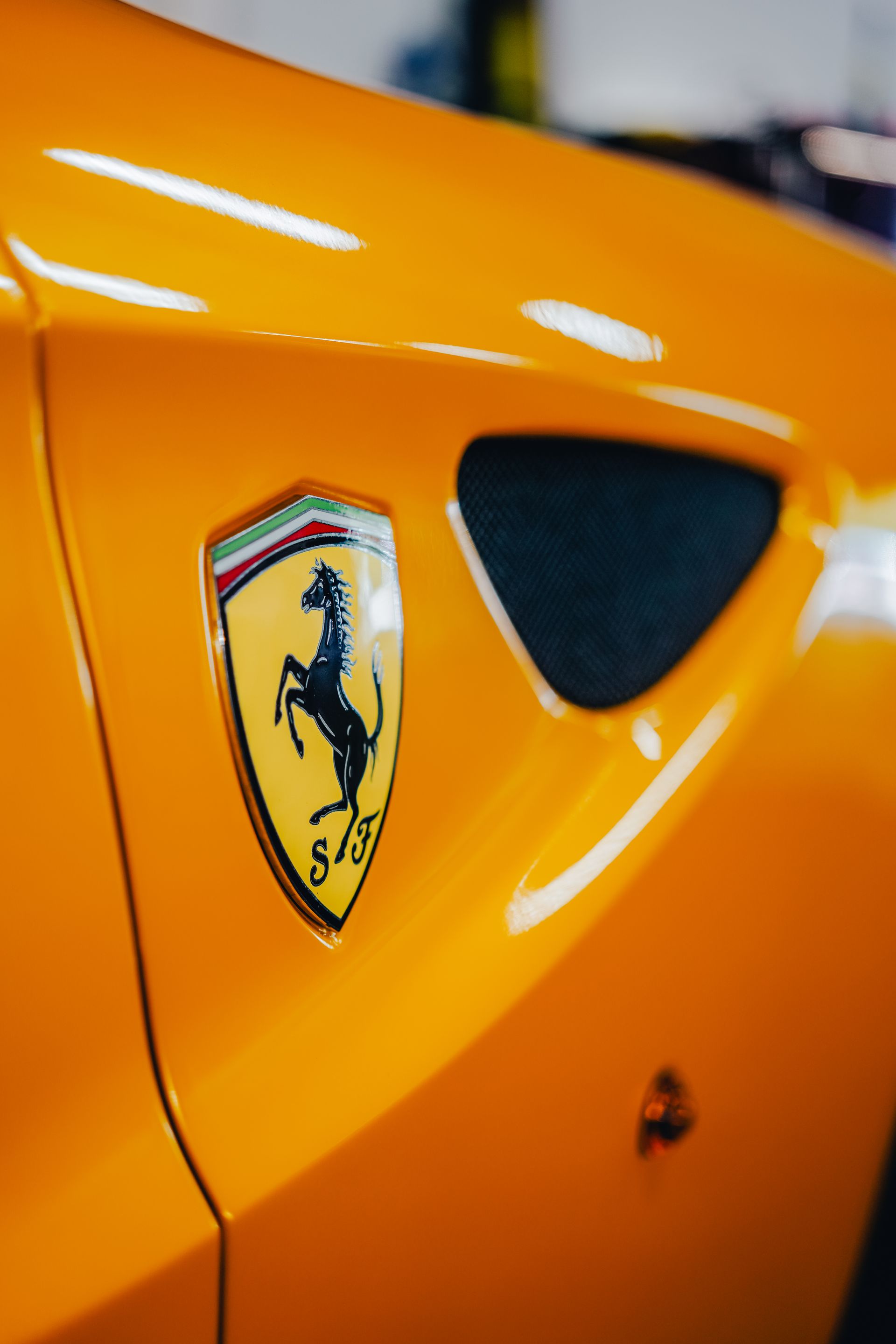 Close-up of a yellow Ferrari badge on an orange sports car body.