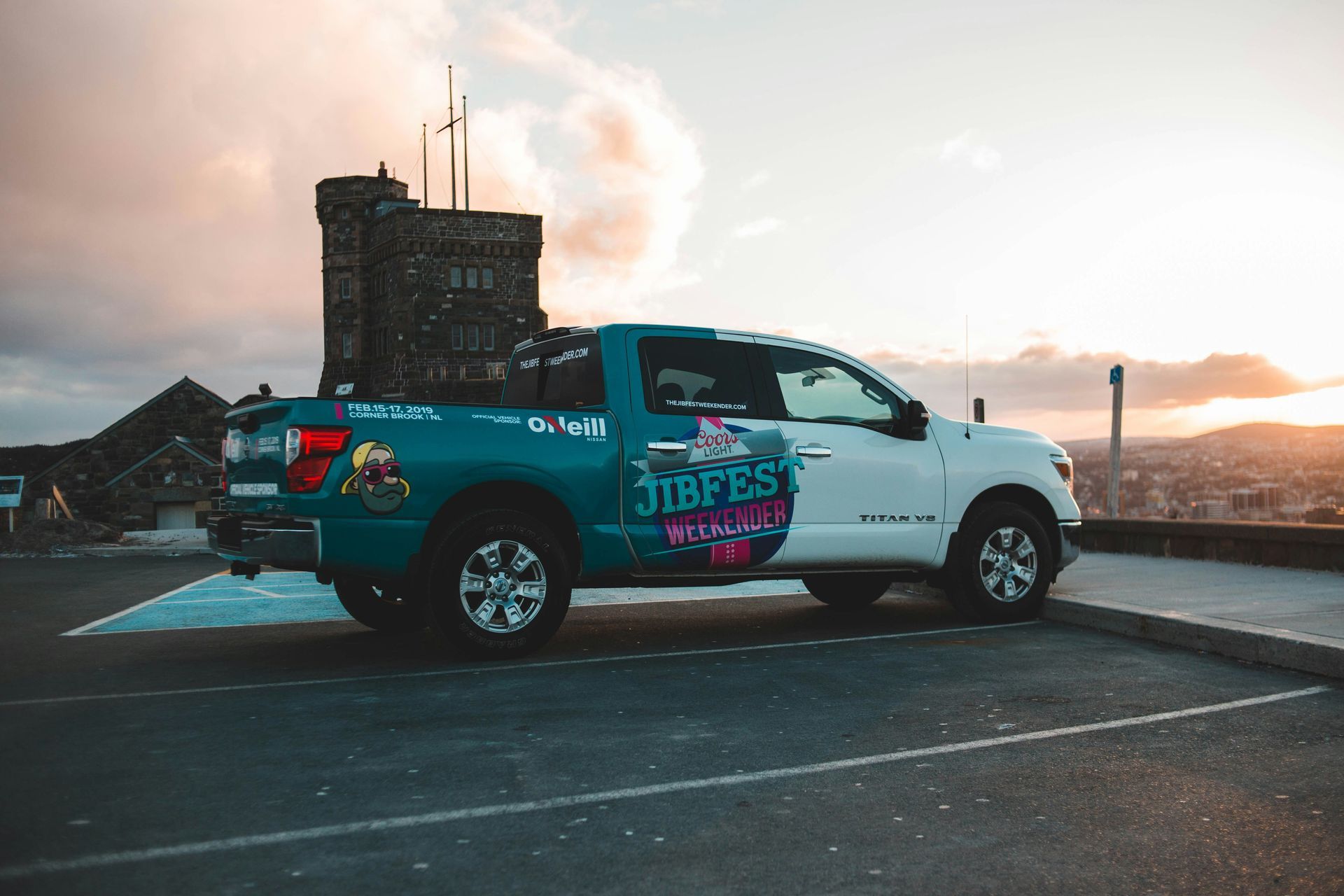 White pickup truck with colorful graphic wrap parked at sunset near a stone tower and waterfront