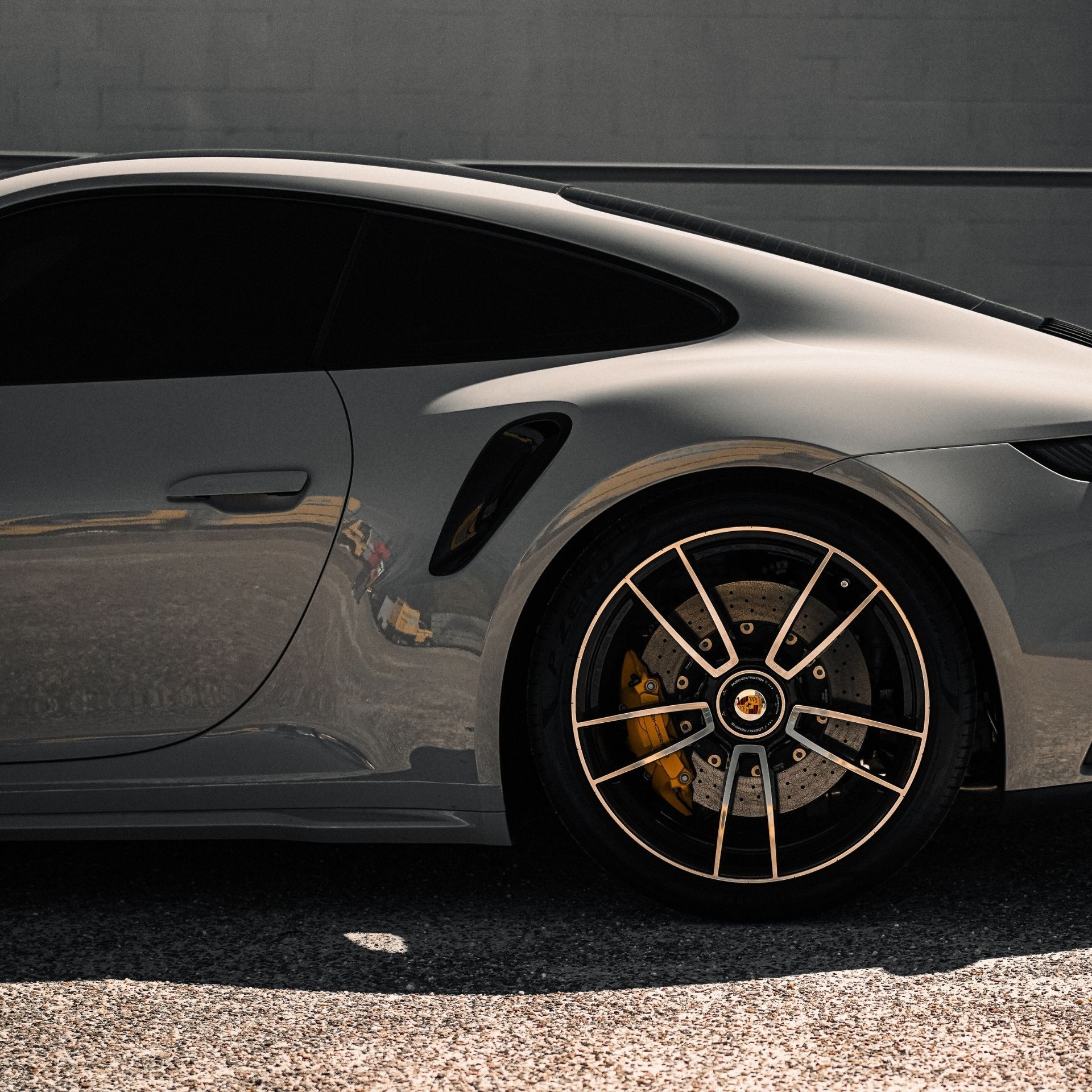 Side view of a silver sports car with black-tinted windows and gold-accented wheels.