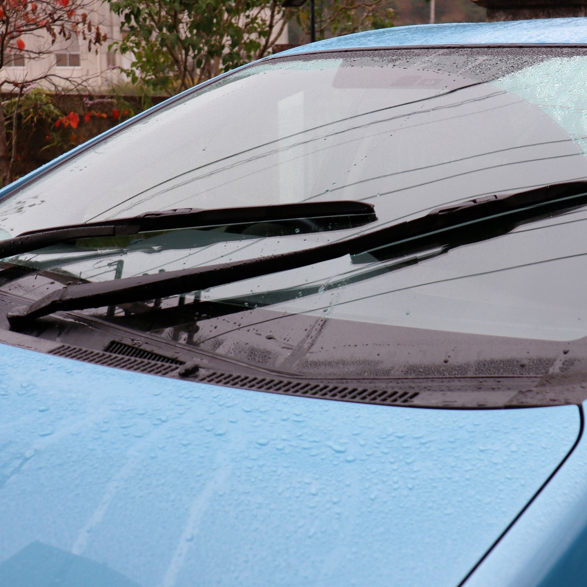 Rain-speckled blue car windshield with windshield wipers visible