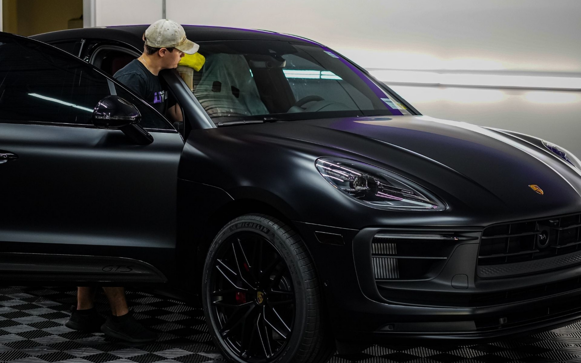 Black Porsche SUV in a garage with a person leaning out the driver’s door checking it