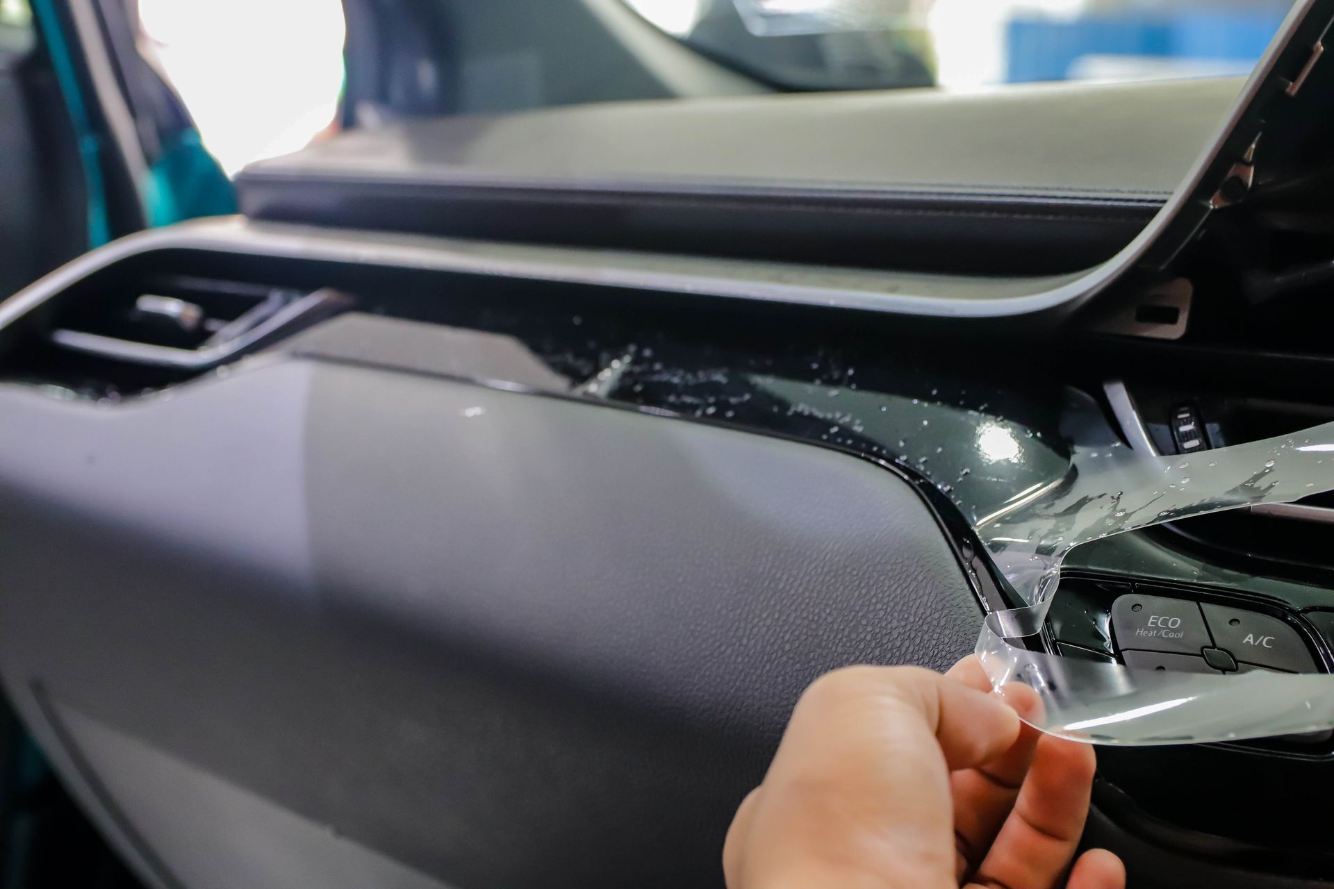 Hand peeling clear protective film from a glossy black car interior dashboard panel