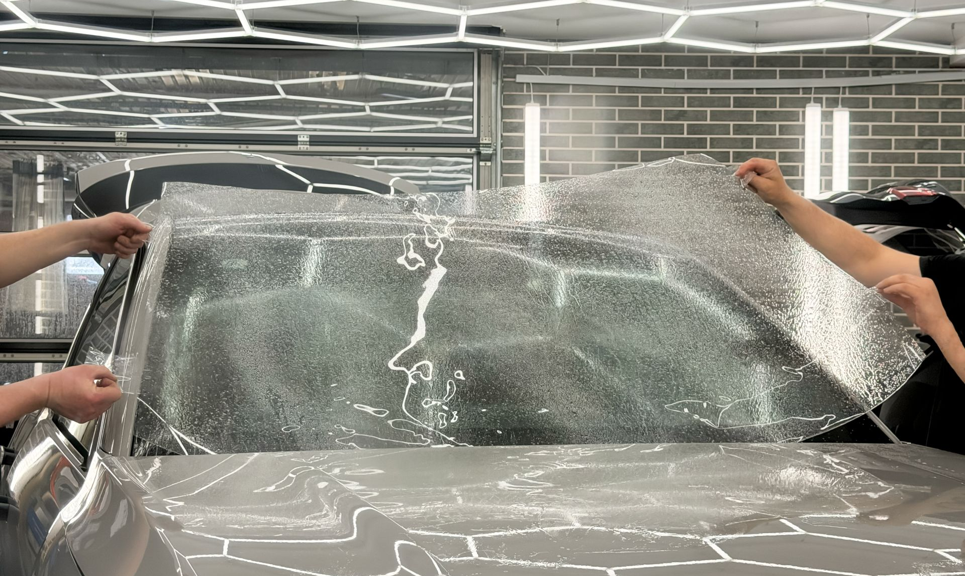 People opening a car windshield with water splashing in a garage