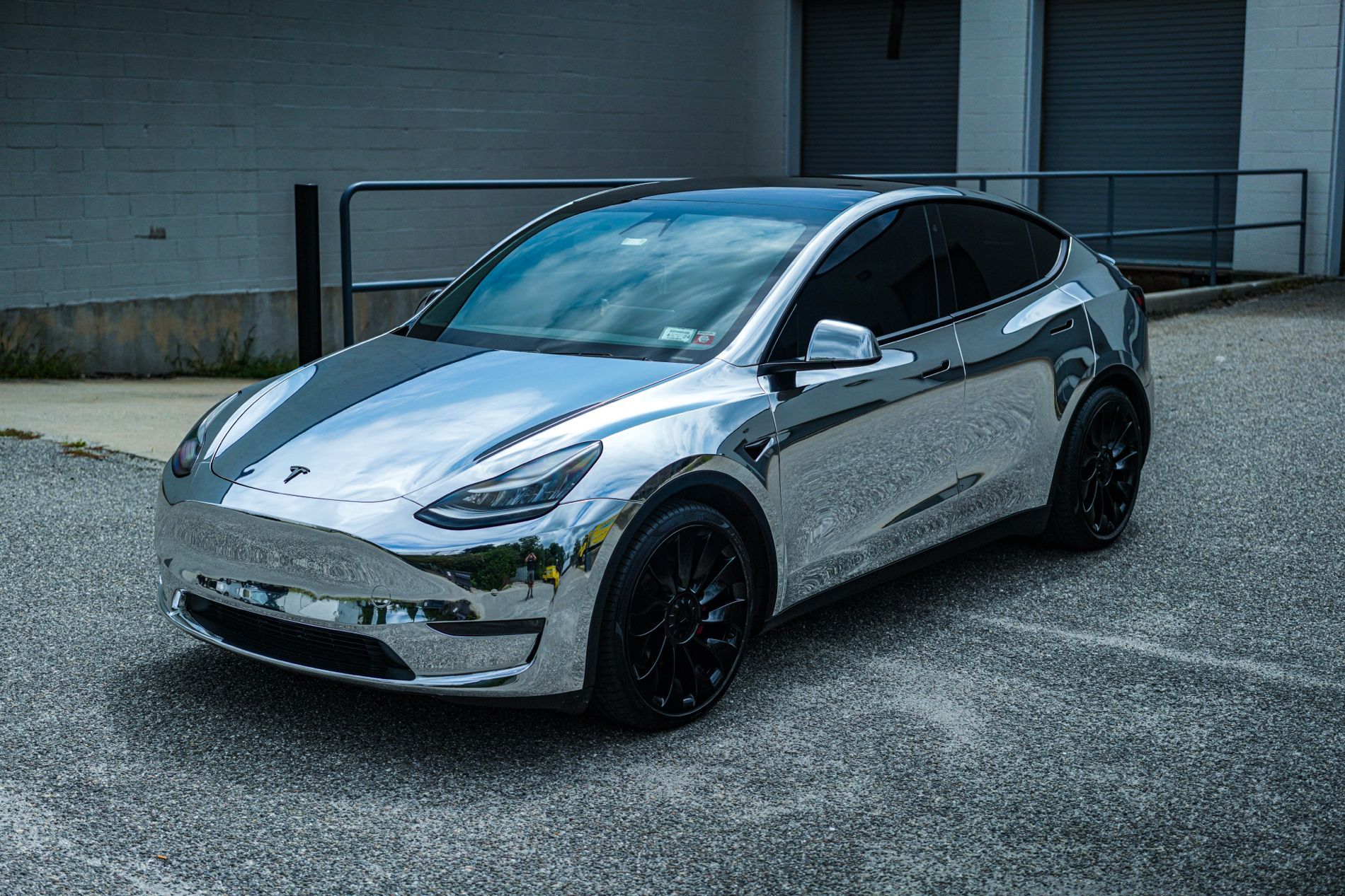 Chrome Tesla Model 3 parked on gravel outside a building