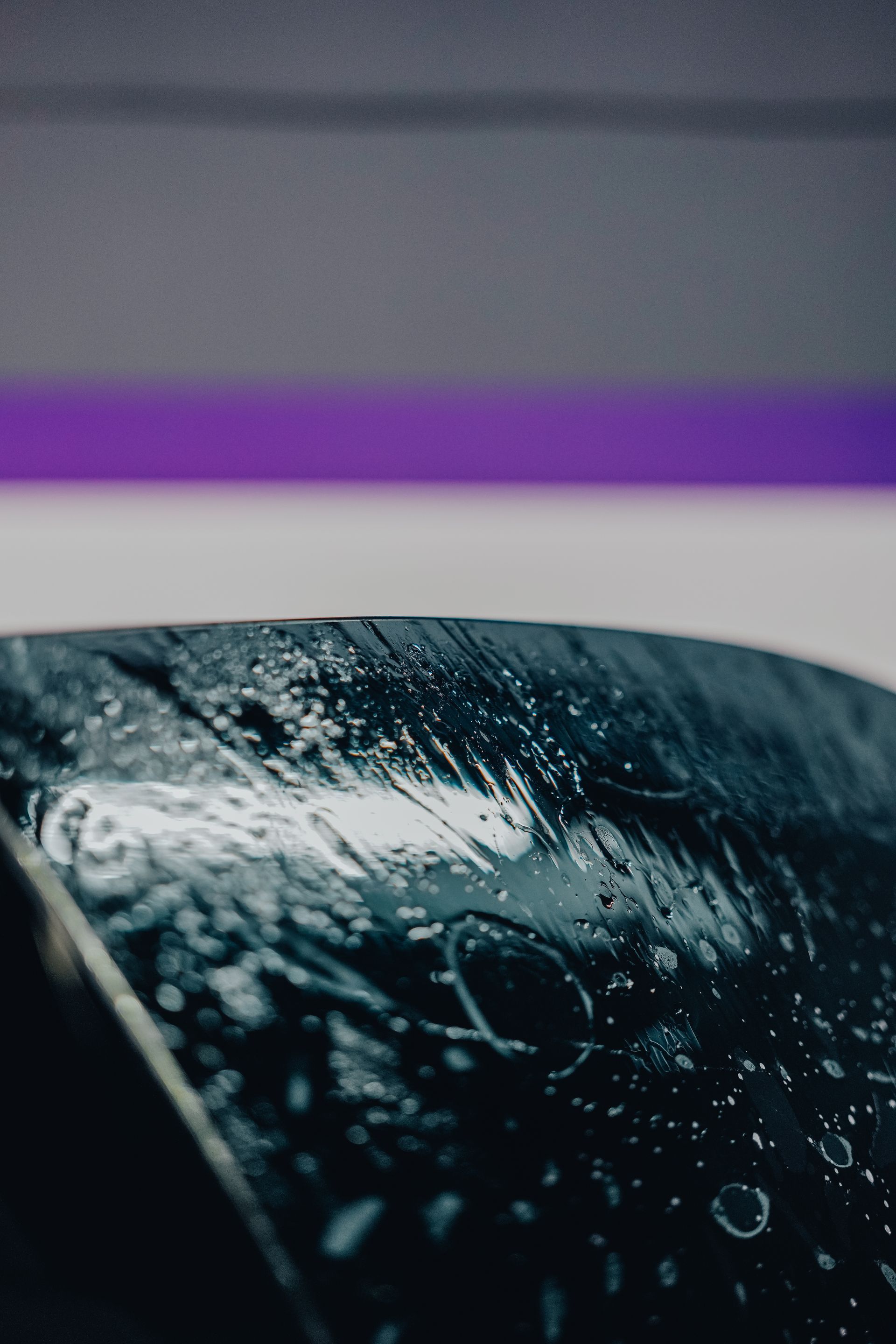 Rain-speckled car windshield with a blurred purple light reflection at the top