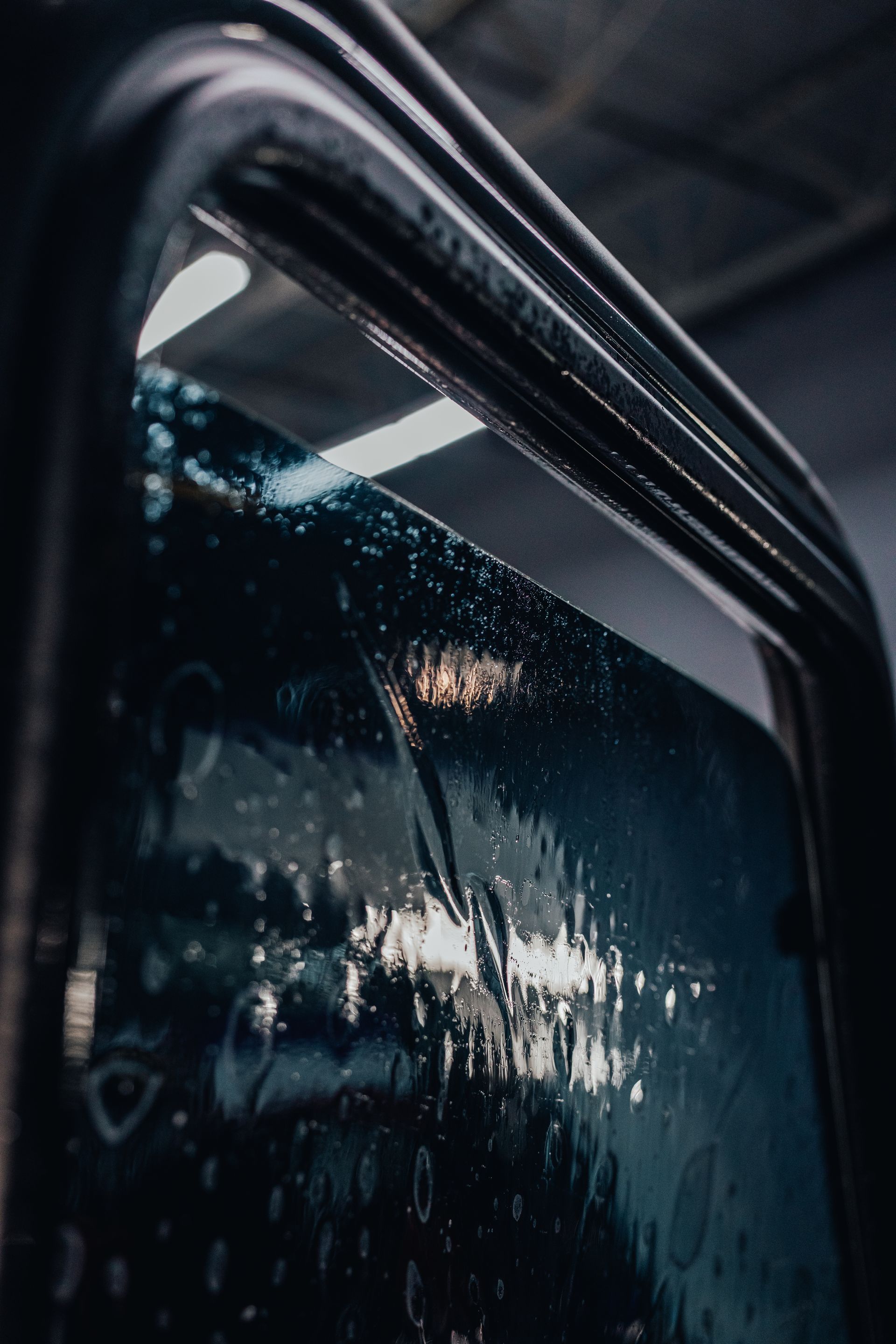 Close-up of a wet bus window with water droplets and reflections in dim light