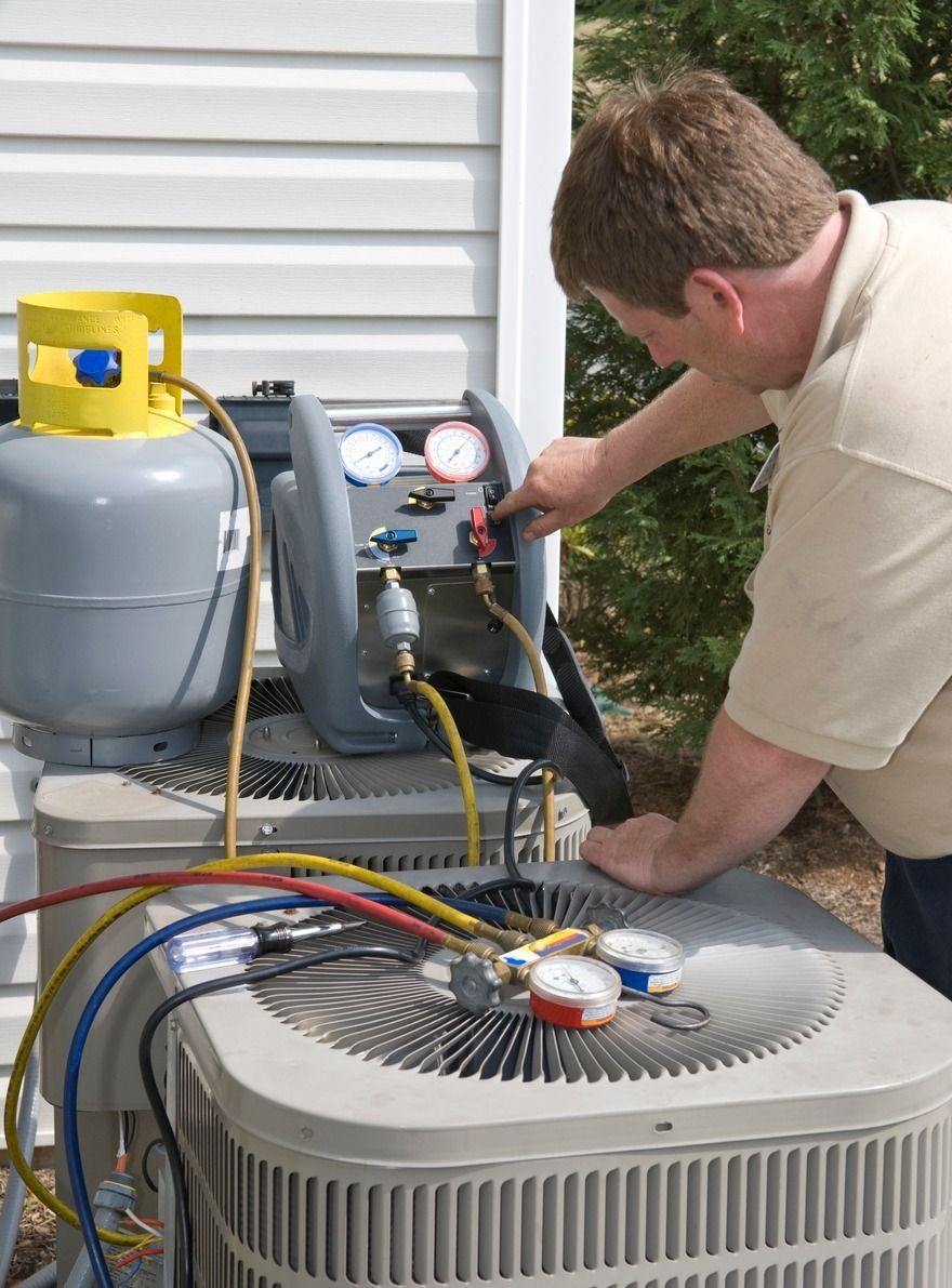 A technician operates a portable HVAC recovery machine connected to an outdoor air conditioning unit with colored hoses.