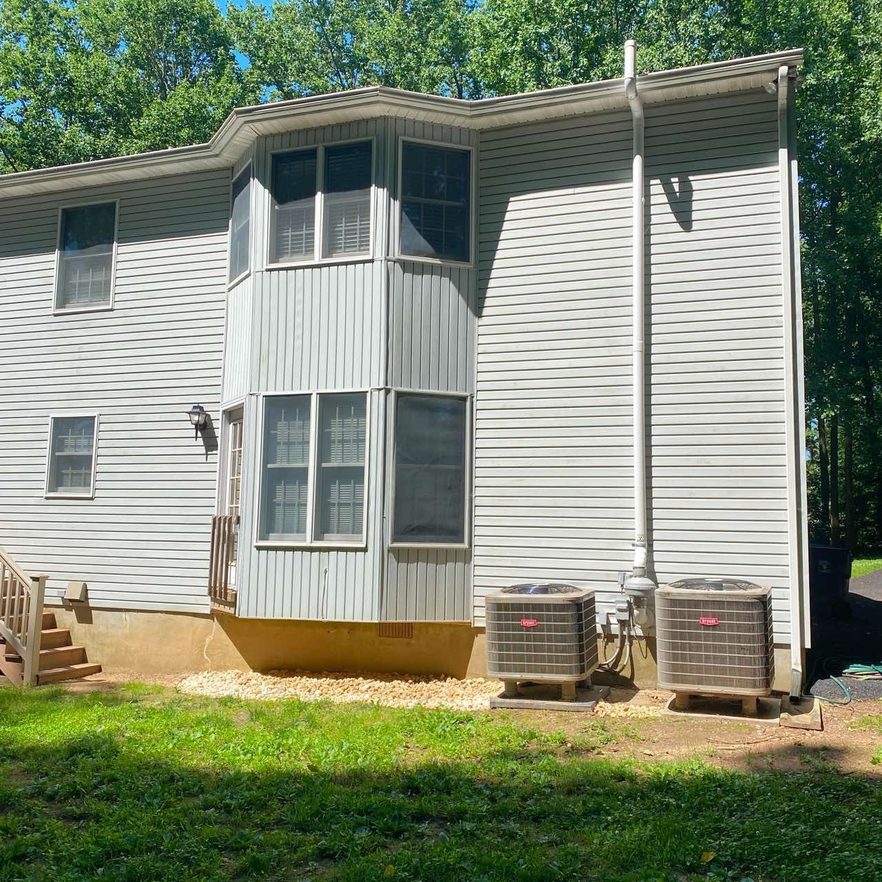 Exterior of a two-story house with light grey vinyl siding, a bay window, and two outdoor HVAC units in a grassy yard.