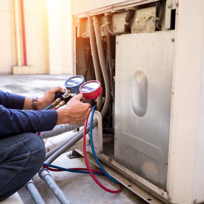 A technician uses a manifold gauge set to check refrigerant pressure on an outdoor HVAC unit.
