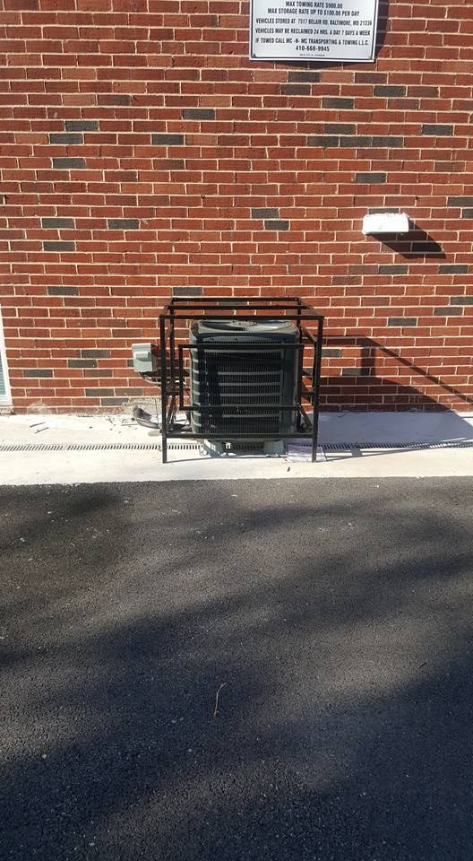 An outdoor HVAC unit enclosed in a black metal security cage against a red brick wall.
