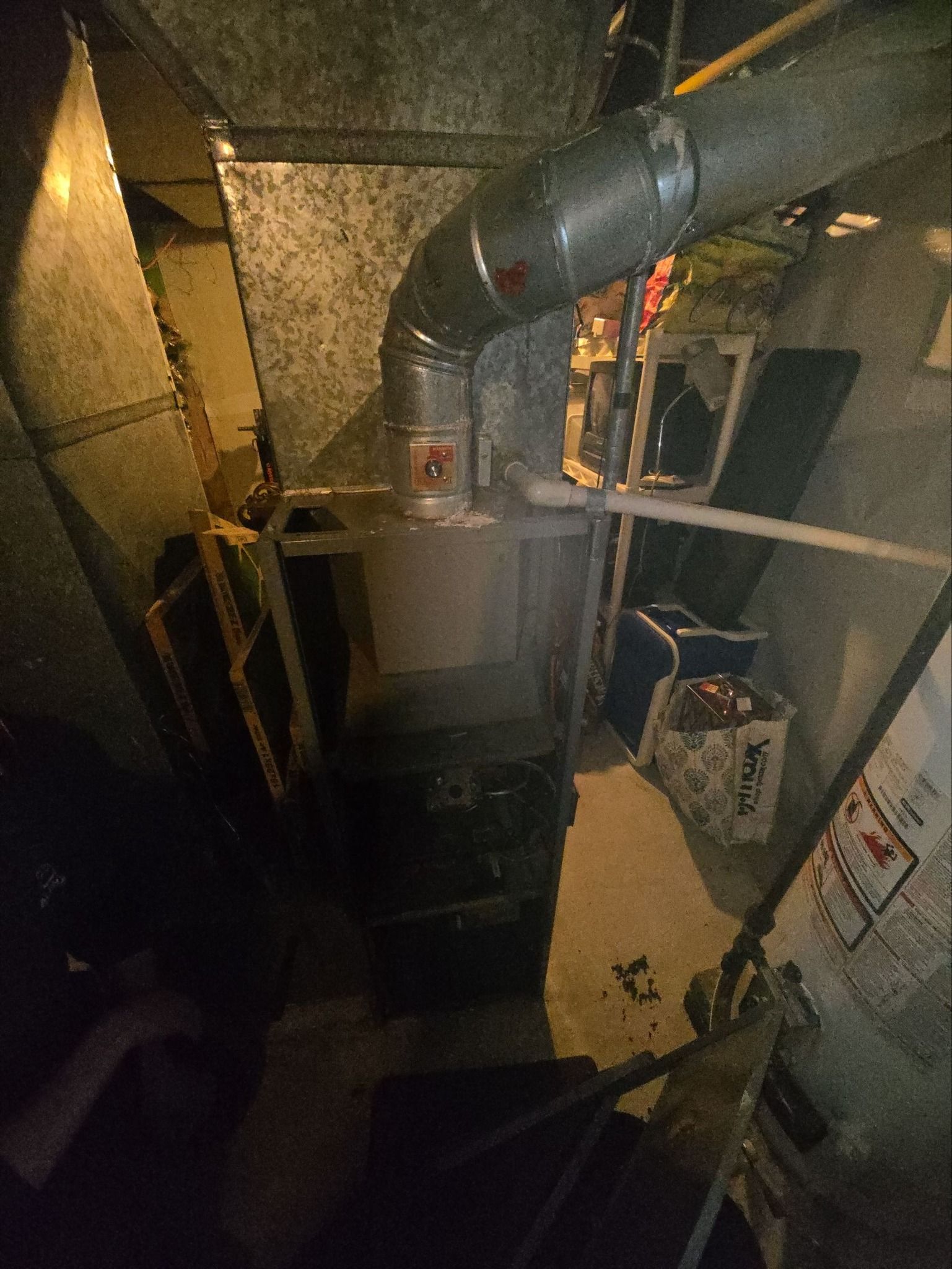 A central residential furnace in a cluttered basement, with silver metal ducting extending from the top.