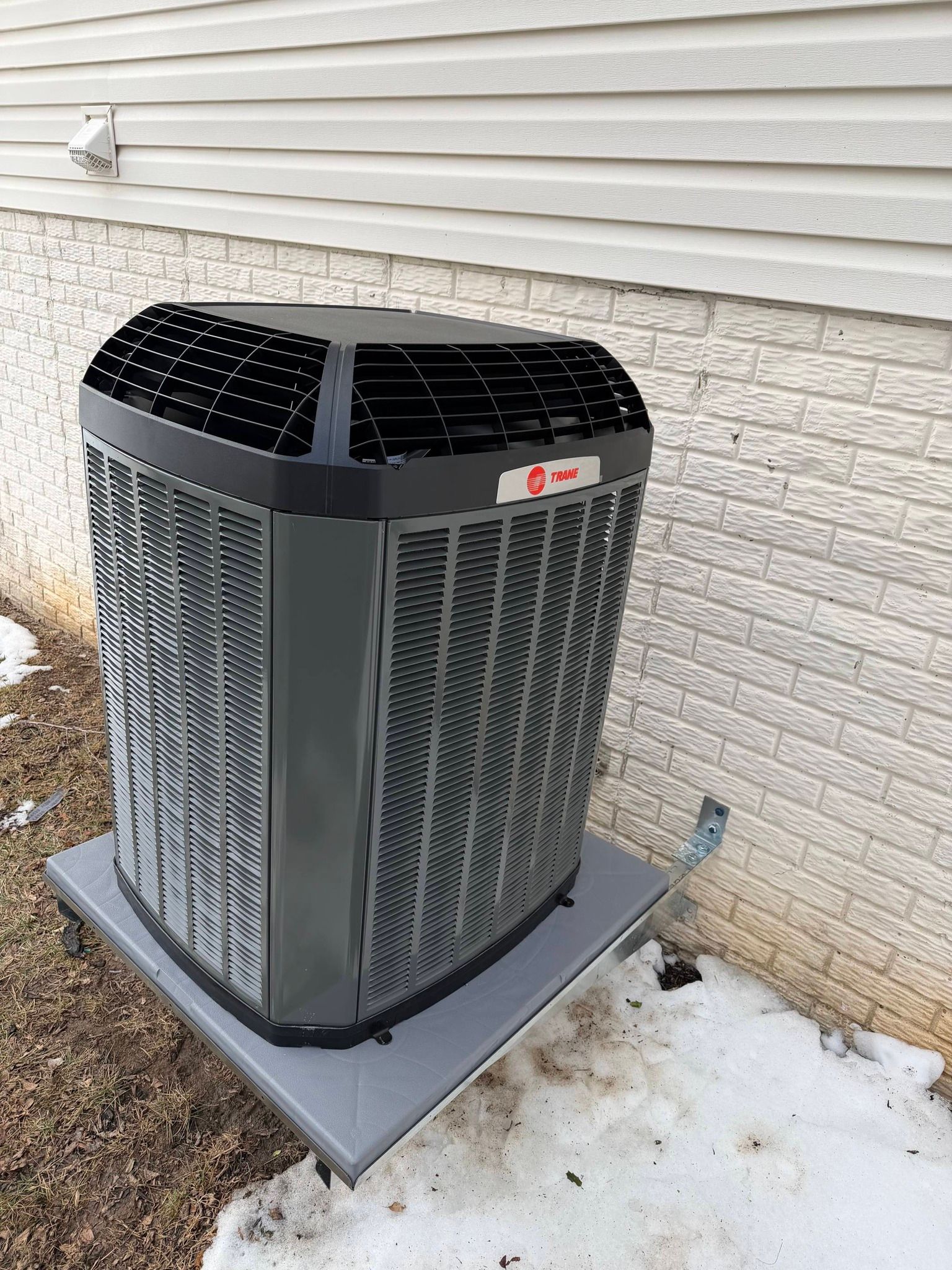 An outdoor HVAC unit on a brick wall foundation, connected to a vacuum pump and diagnostic gauges during a repair.