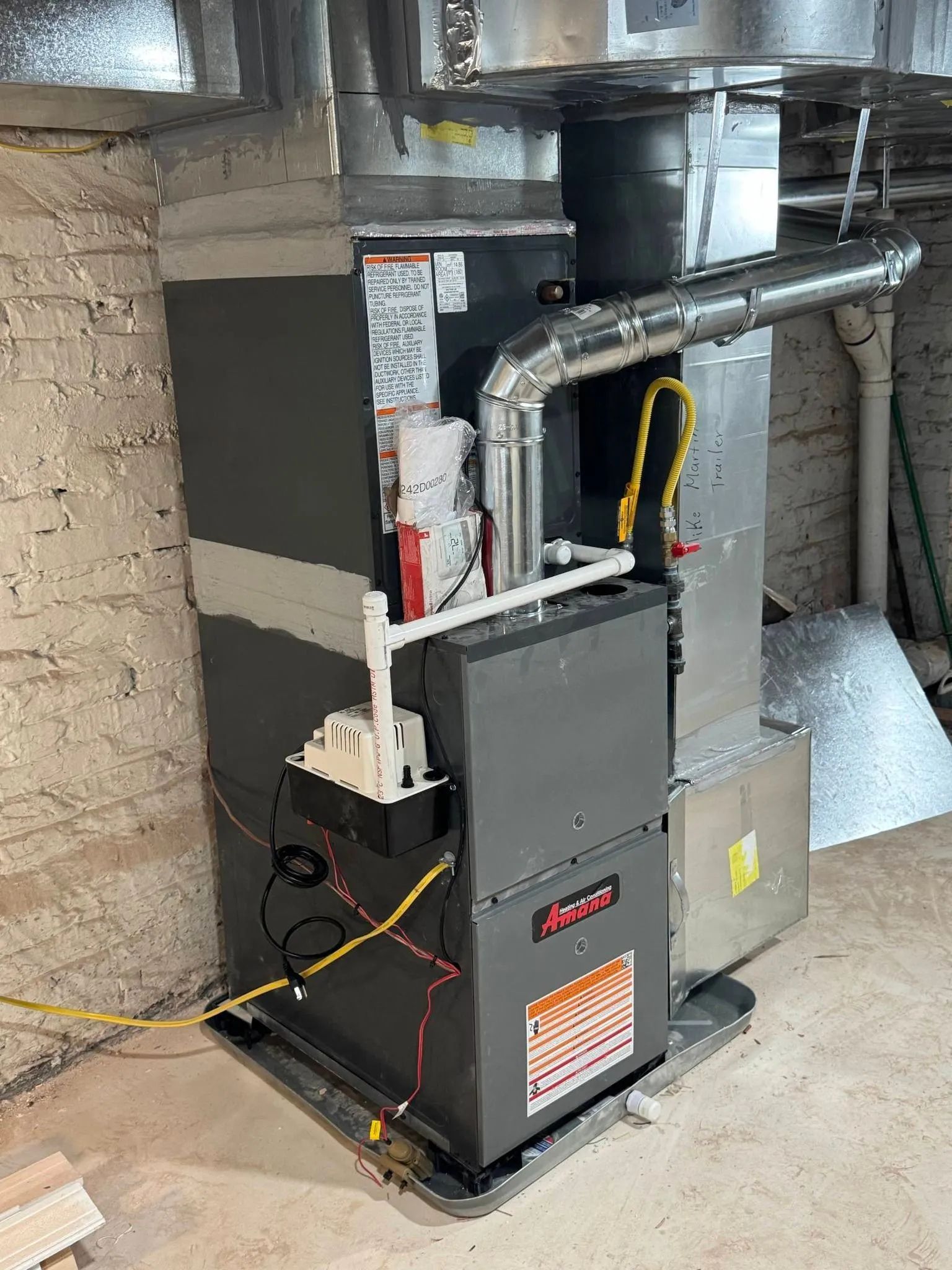 Gas furnace and ductwork in a basement utility area, with exposed pipes and a yellow extension cord.