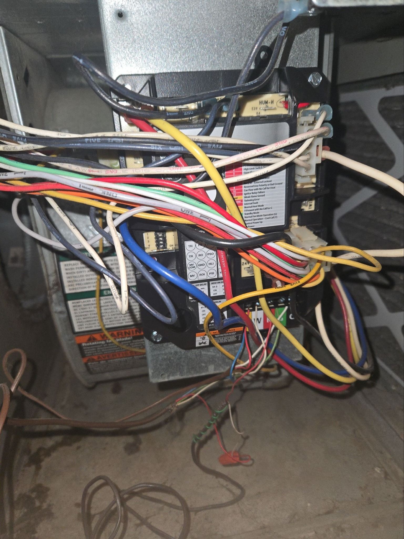 A tangled cluster of colorful electrical wires and components connected to an HVAC control board inside a furnace unit.