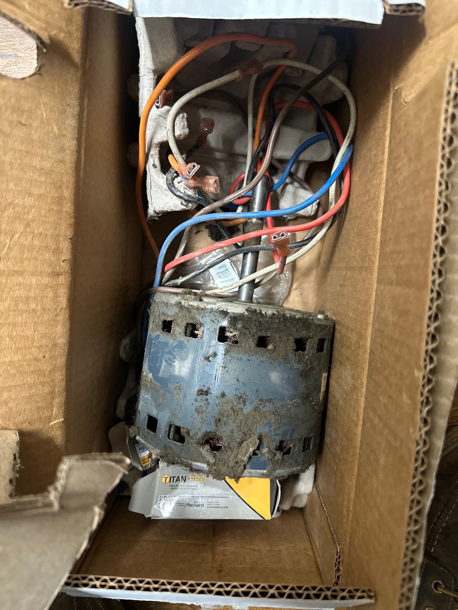 An electric motor with exposed wiring sits inside a brown cardboard shipping box.