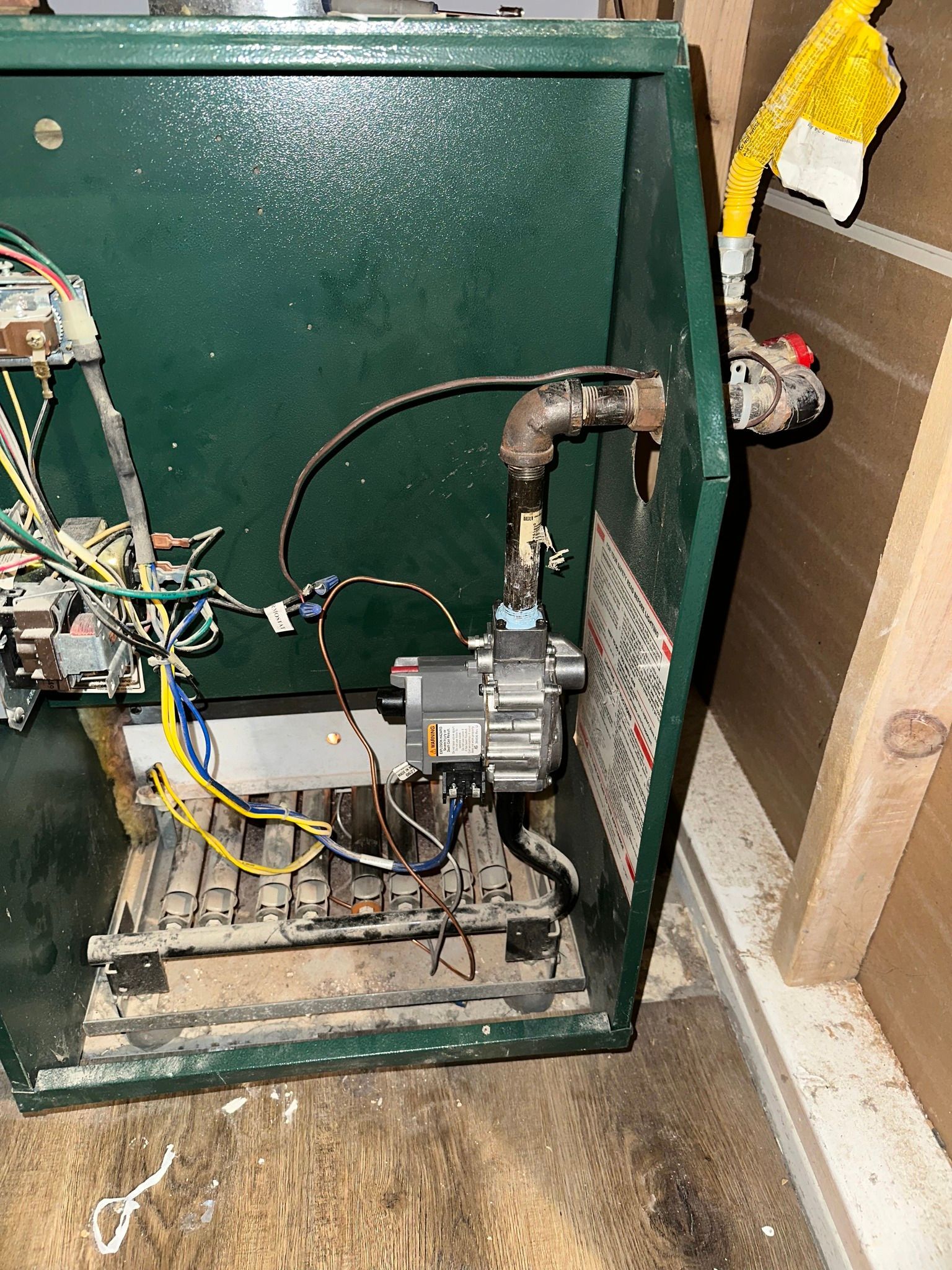 An open green metal casing reveals the internal components, gas lines, and wiring of a residential furnace unit.