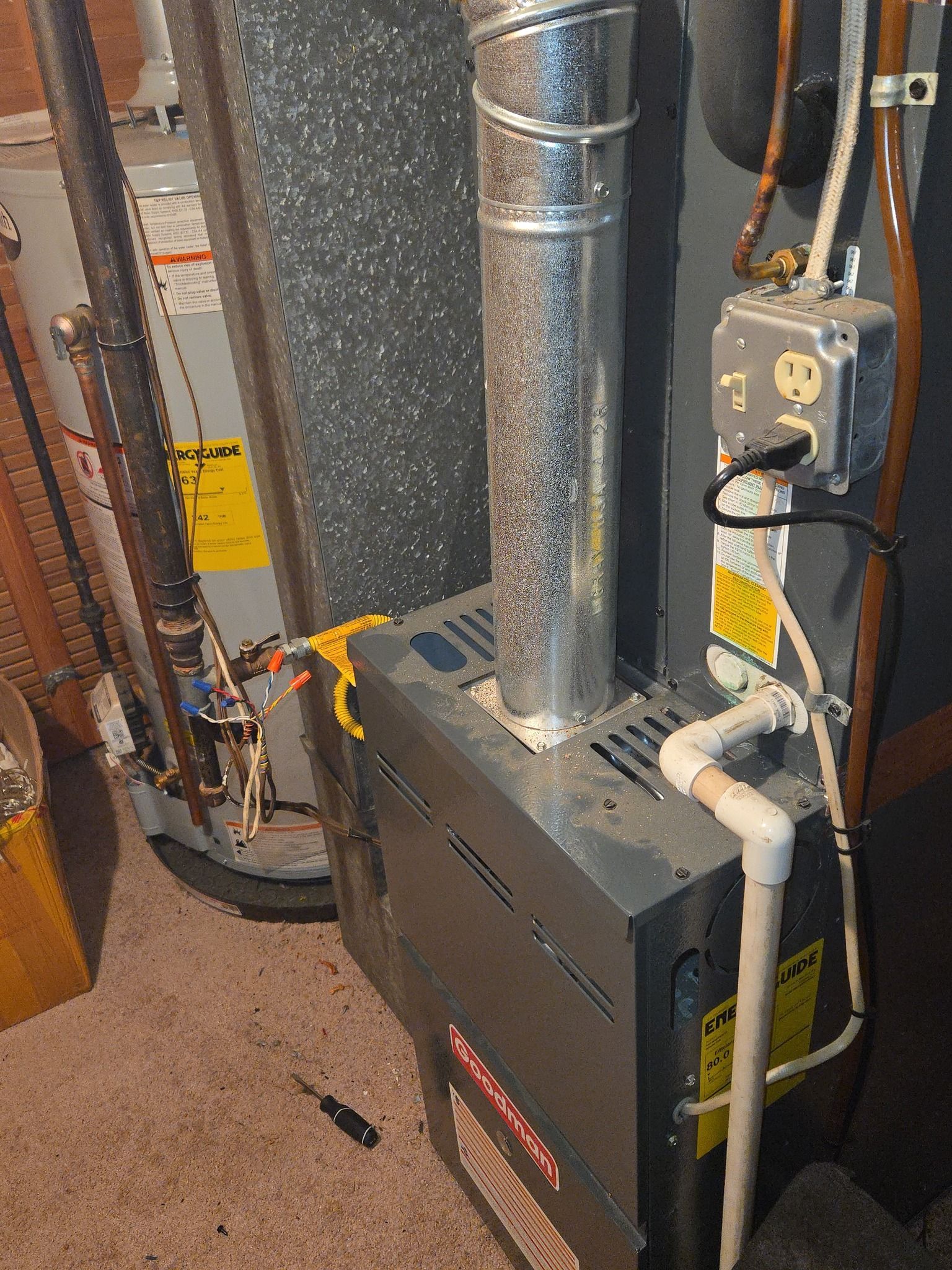 Three gray HVAC condenser units sit on a concrete pad outside a tan-sided building with a brick stone foundation.