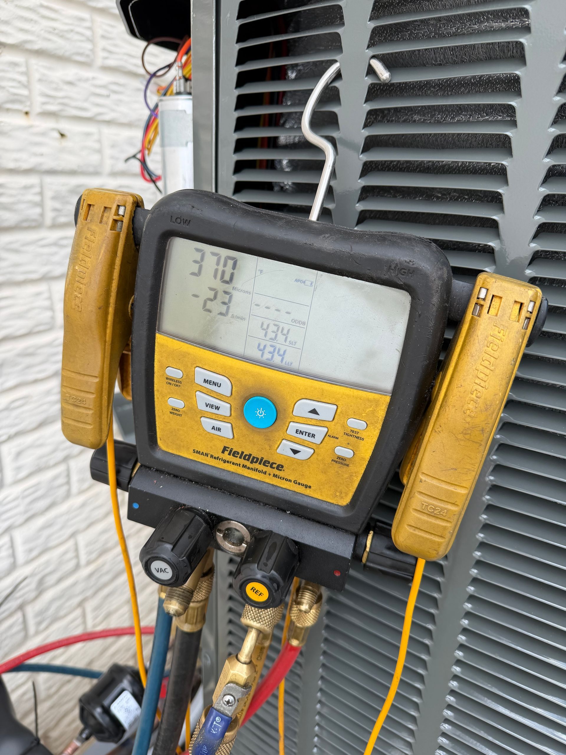 A Fieldpiece digital manifold gauge attached to an outdoor HVAC unit, displaying pressure and temperature readings.