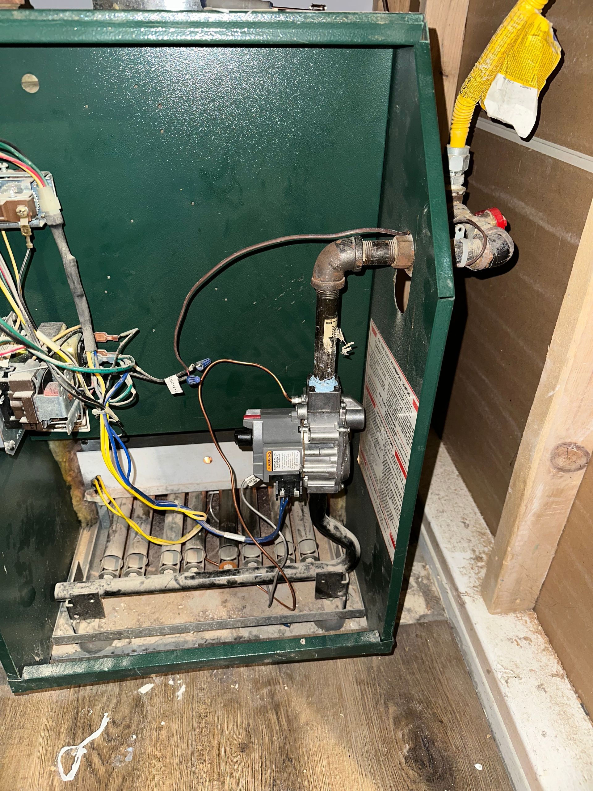 An open, green-cased furnace interior showing internal electrical wiring, a gas valve, and a yellow flexible gas line.