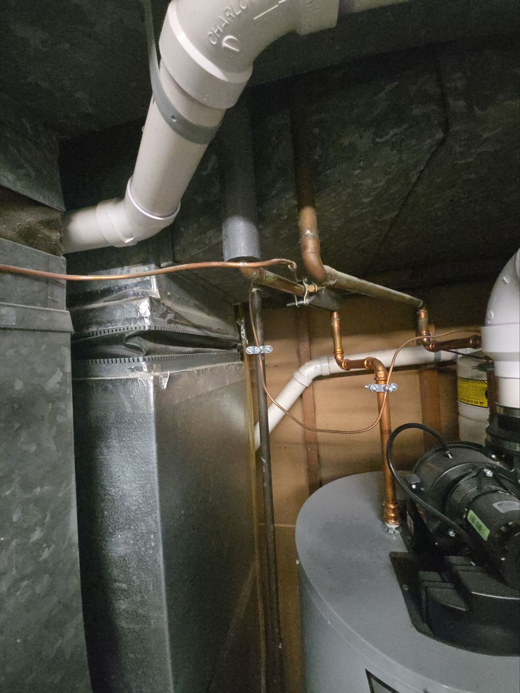 Copper plumbing pipes, white PVC venting, and gray metal ductwork running along a basement ceiling near a water heater.