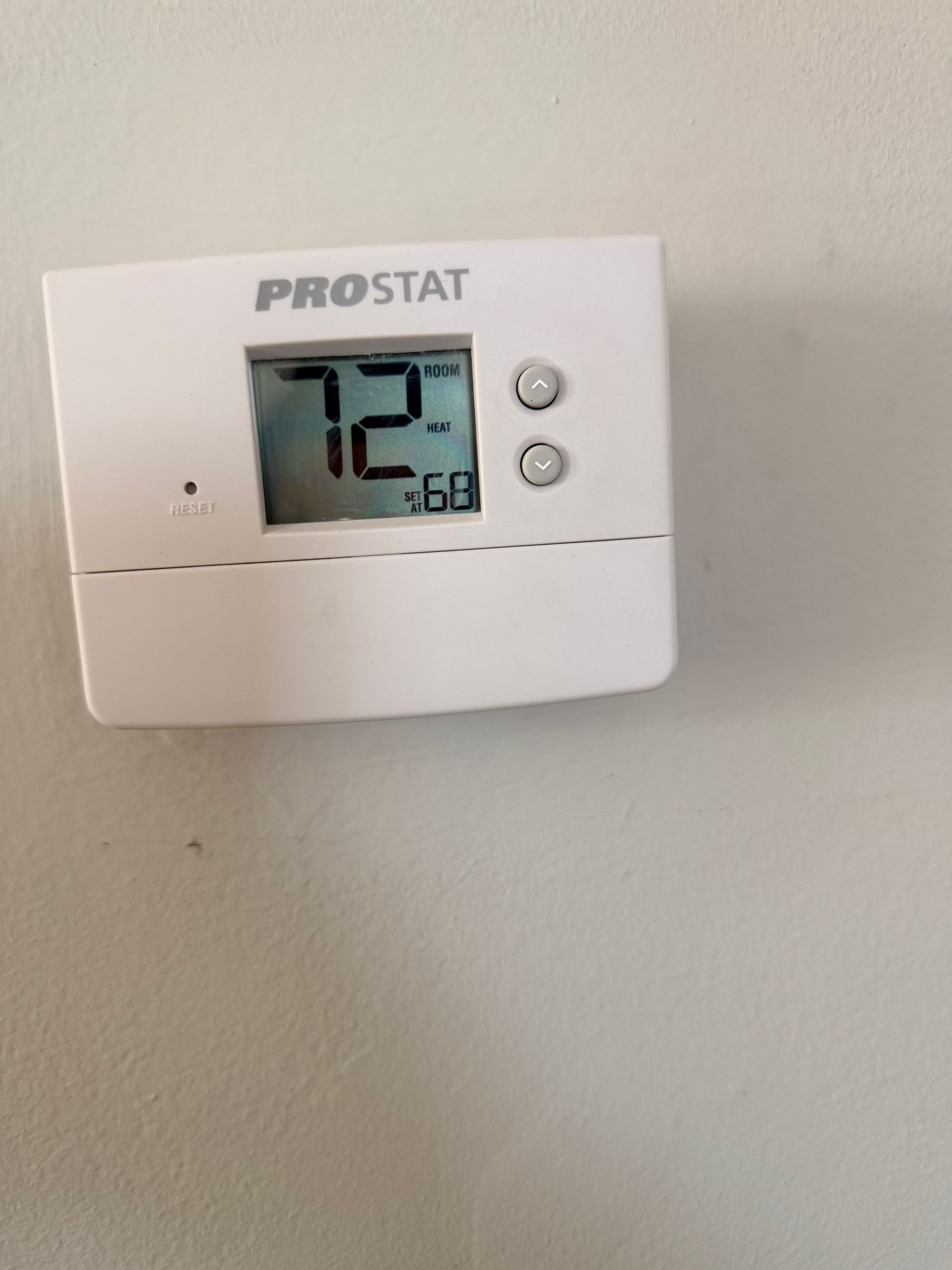 A white Prostat thermostat mounted on a wall displaying 72 degrees Fahrenheit and 58 percent humidity.