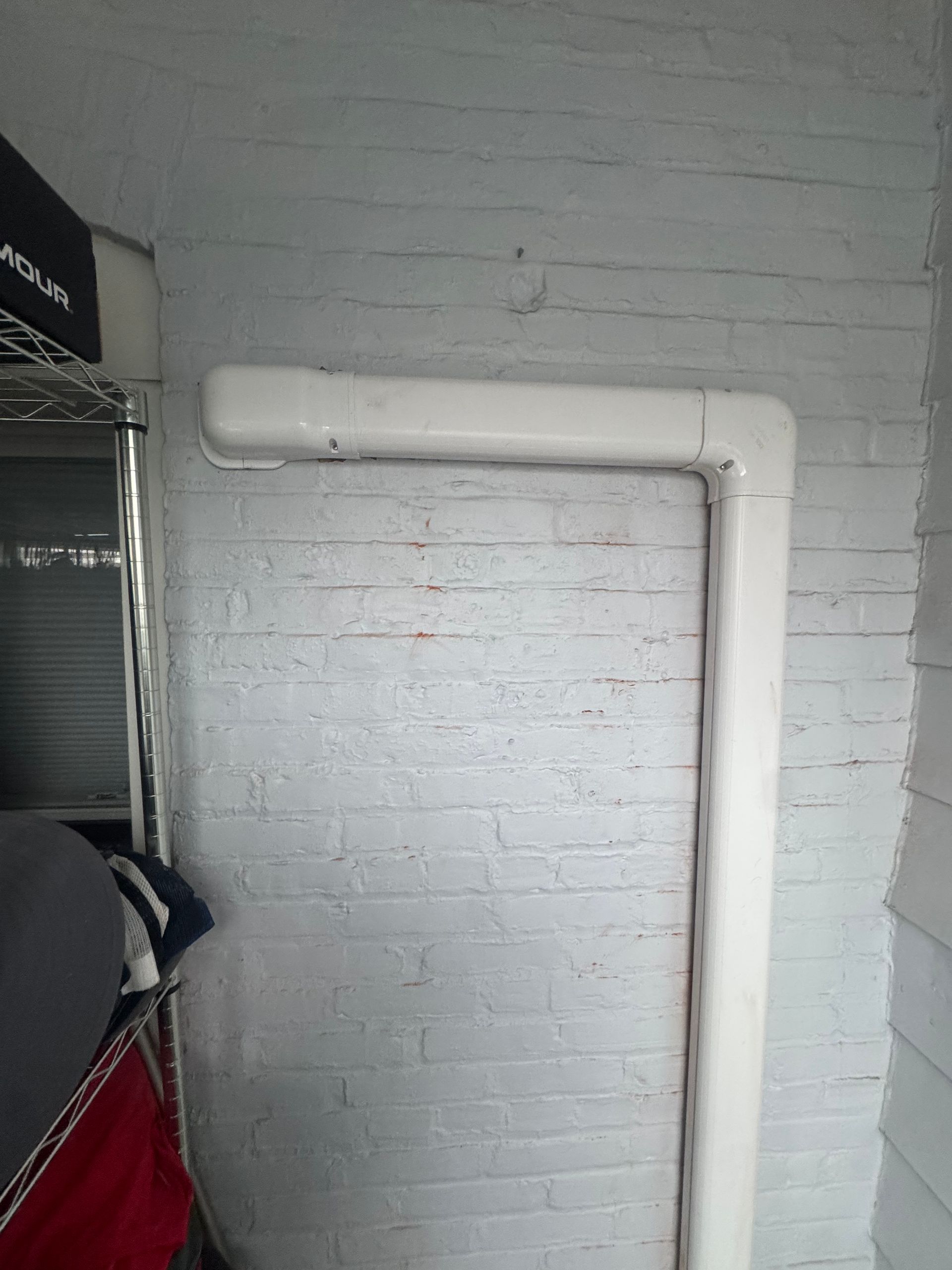 A white PVC pipe runs vertically and turns at a 90-degree angle against a painted white brick wall.