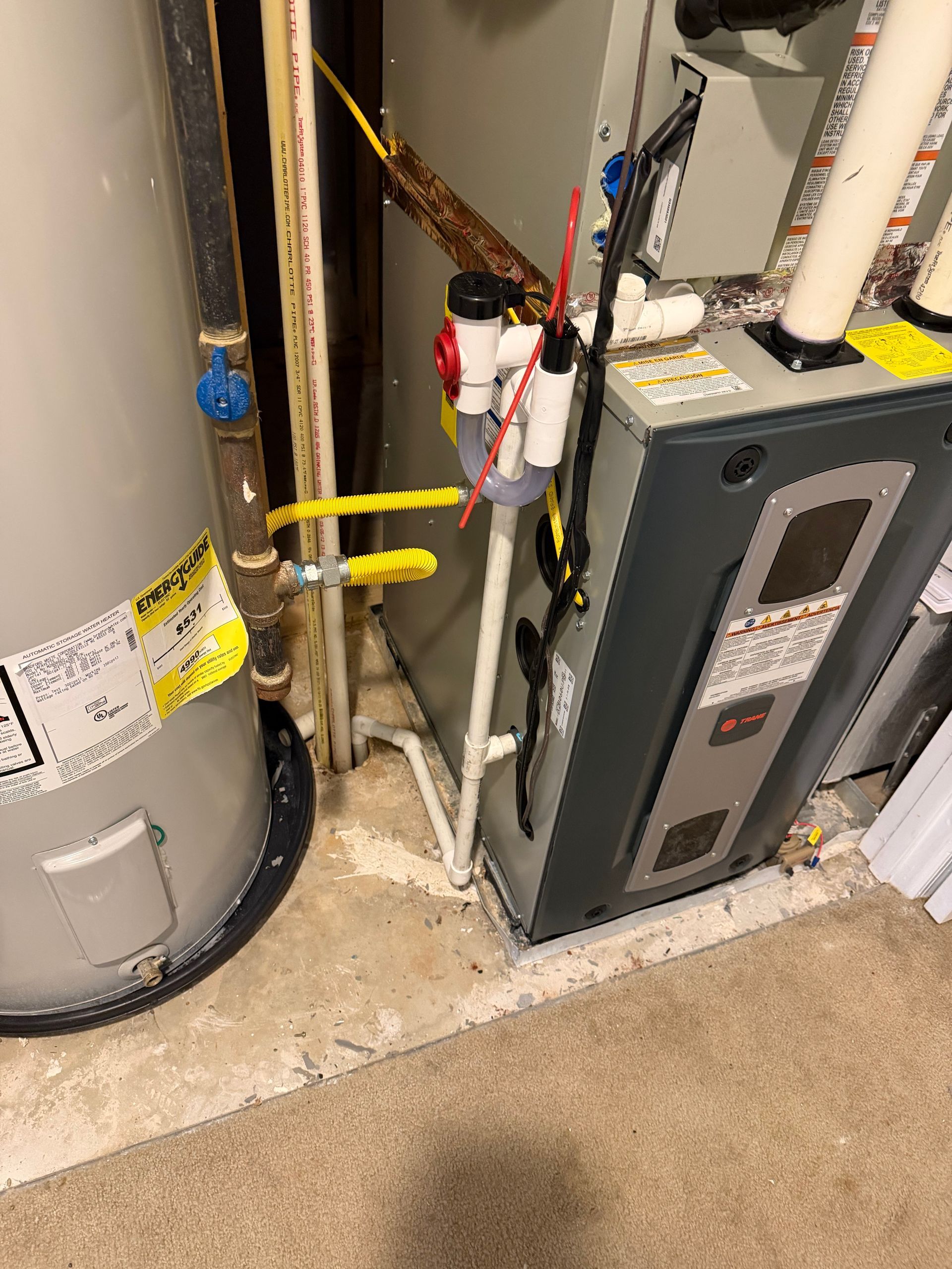 A water heater and a furnace unit standing side by side in a utility closet with white PVC piping and yellow valves.