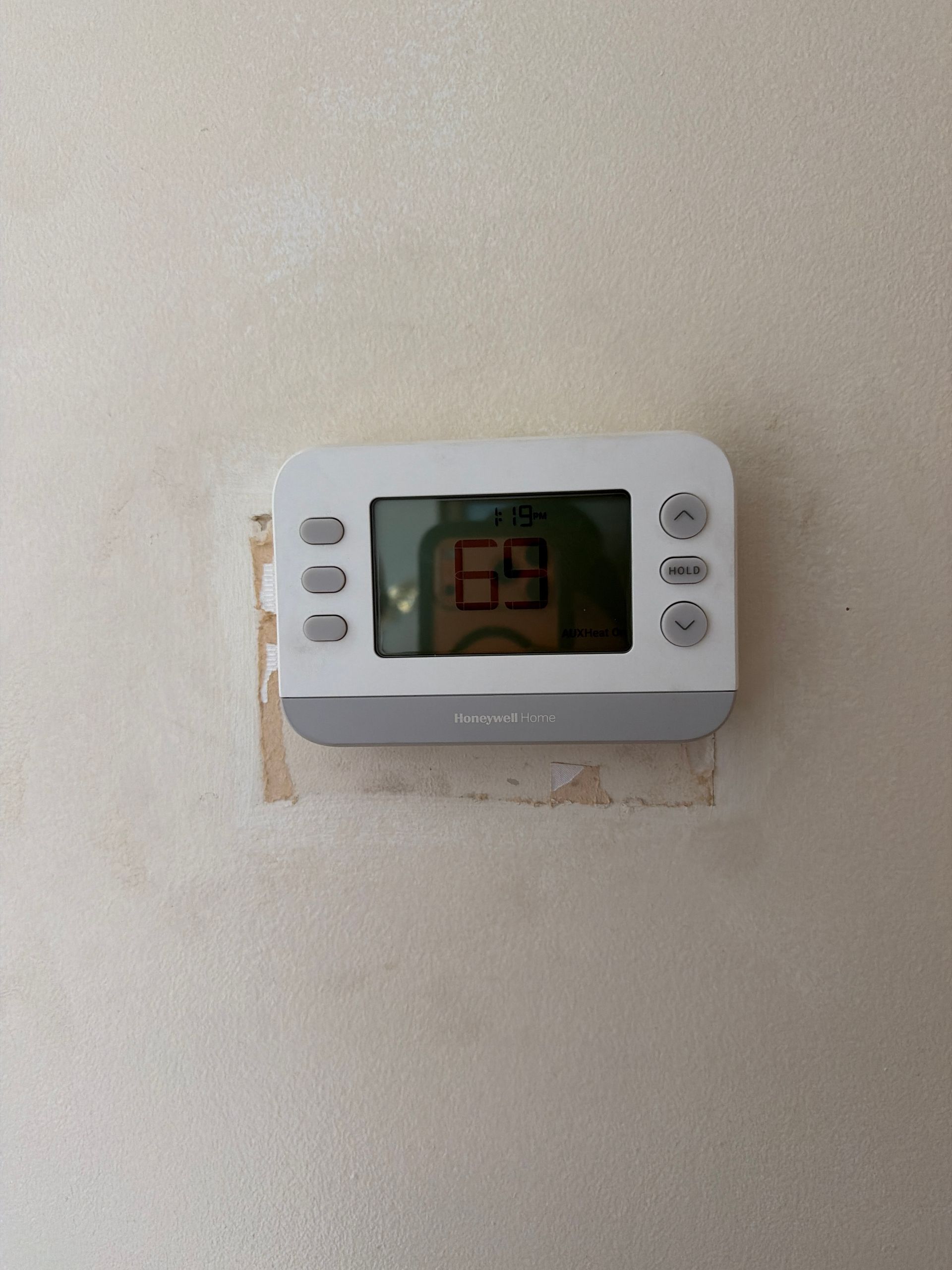 A white digital thermostat mounted on a light-colored wall, displaying a temperature of 69 degrees.