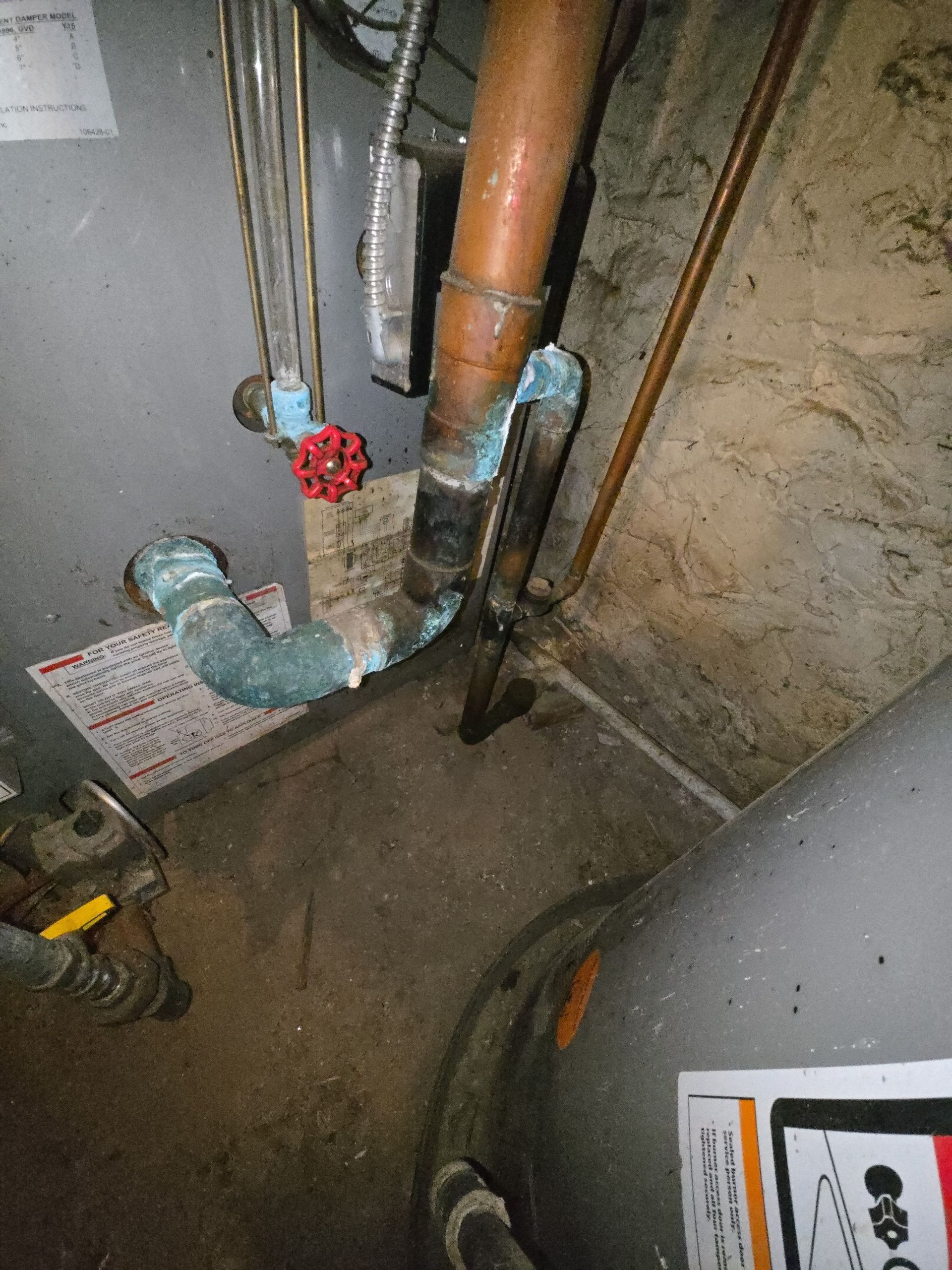 Copper plumbing pipes connected to a water heater showing significant blue-green corrosion at the joints.