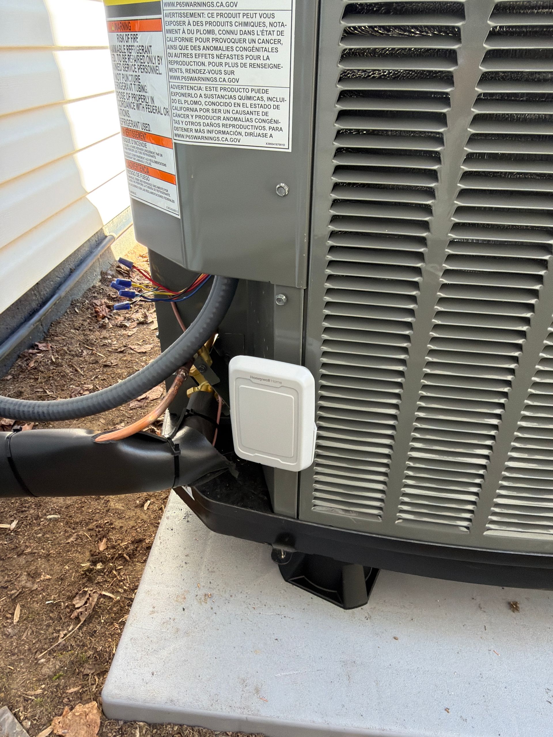 An outdoor air conditioning unit condenser with a white rectangular cover panel, sitting on a concrete pad.