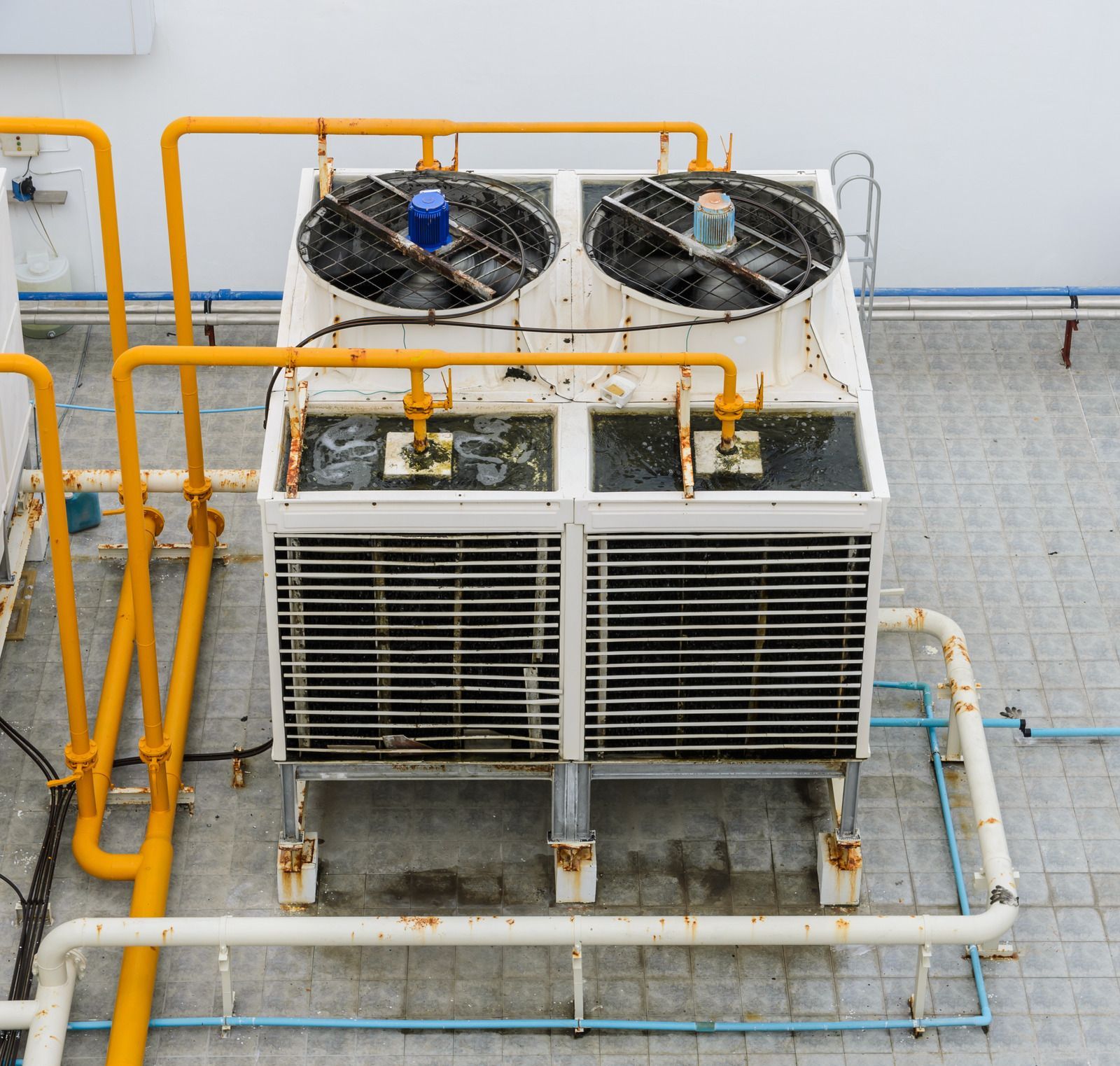 A dual-fan outdoor HVAC unit on a tiled rooftop with connected yellow and white piping.